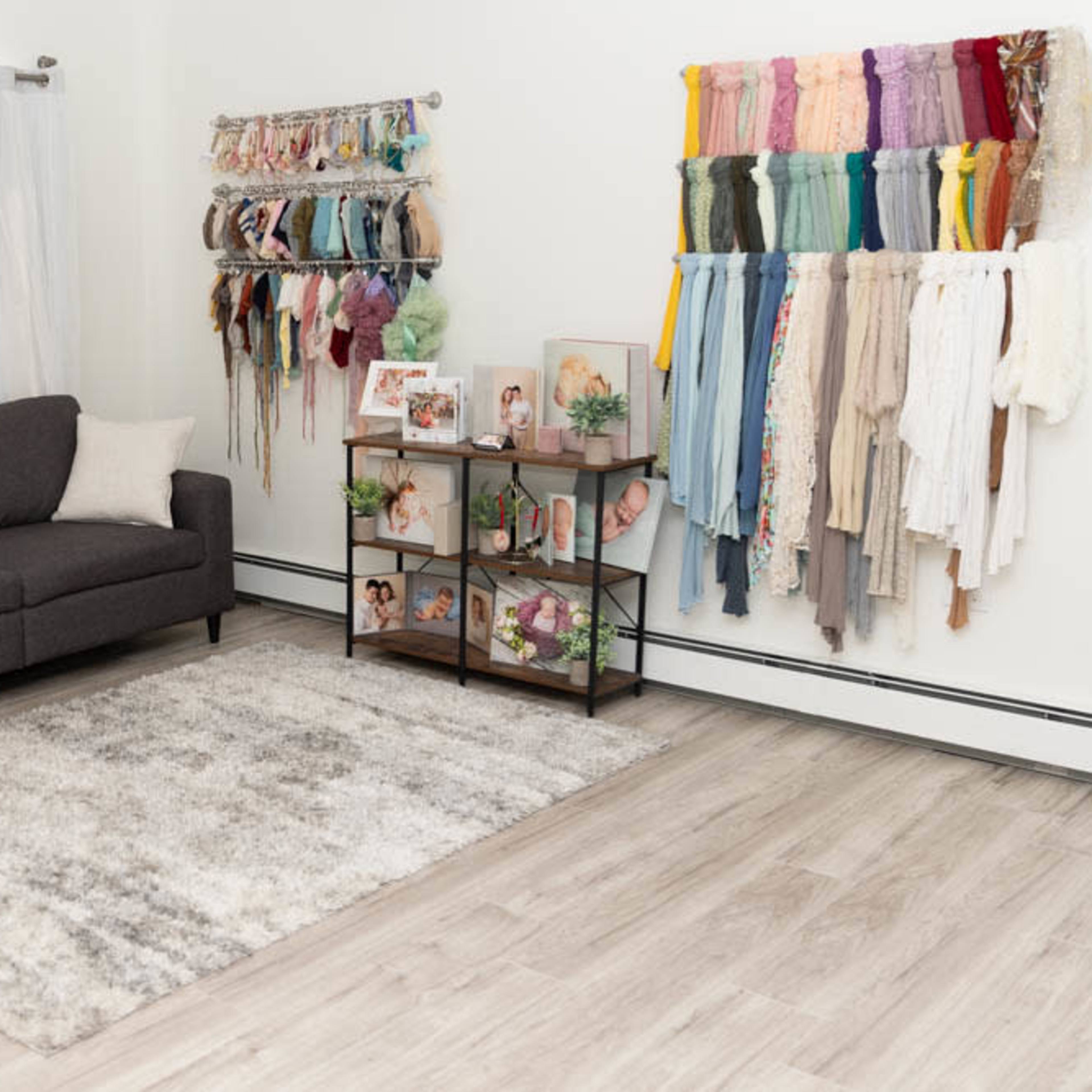 A living room with a gray sofa, a display of colorful fabric swatches on the wall, and a small shelf featuring framed photos and decorative items.