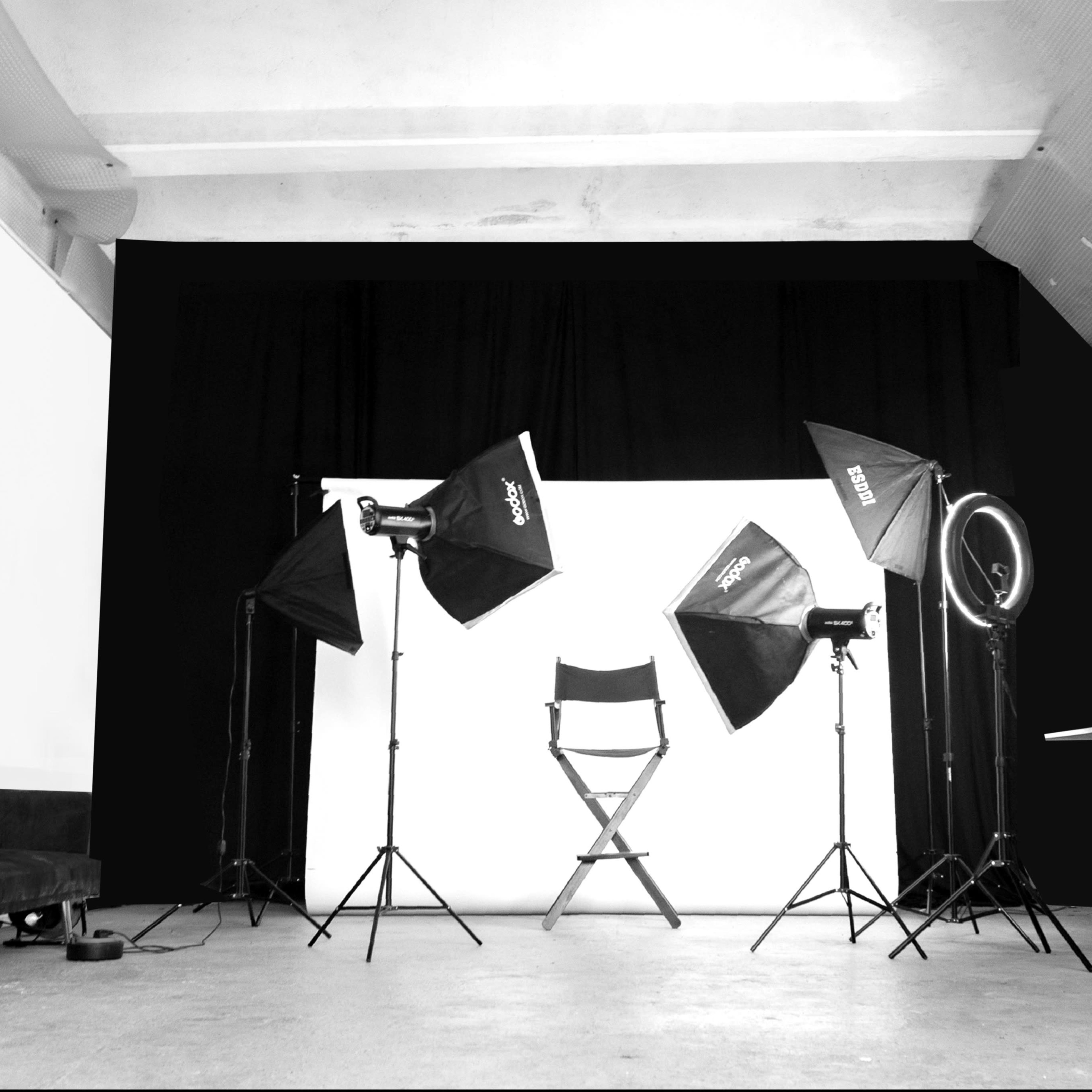A photography studio setup with multiple light sources, a director's chair, and a plain backdrop.