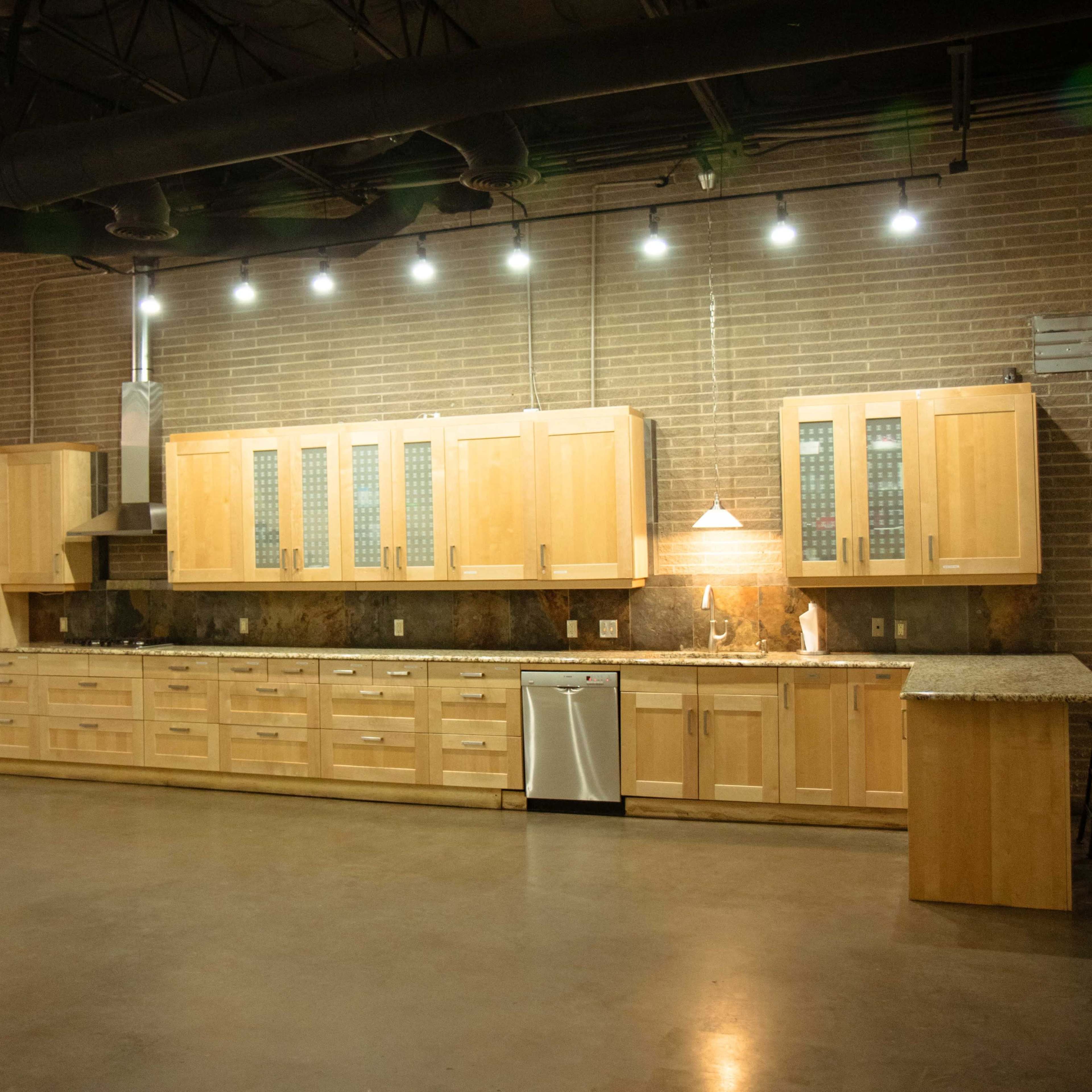 A spacious kitchen with wooden cabinetry, a granite countertop, and stainless steel appliances, set against a brick wall.