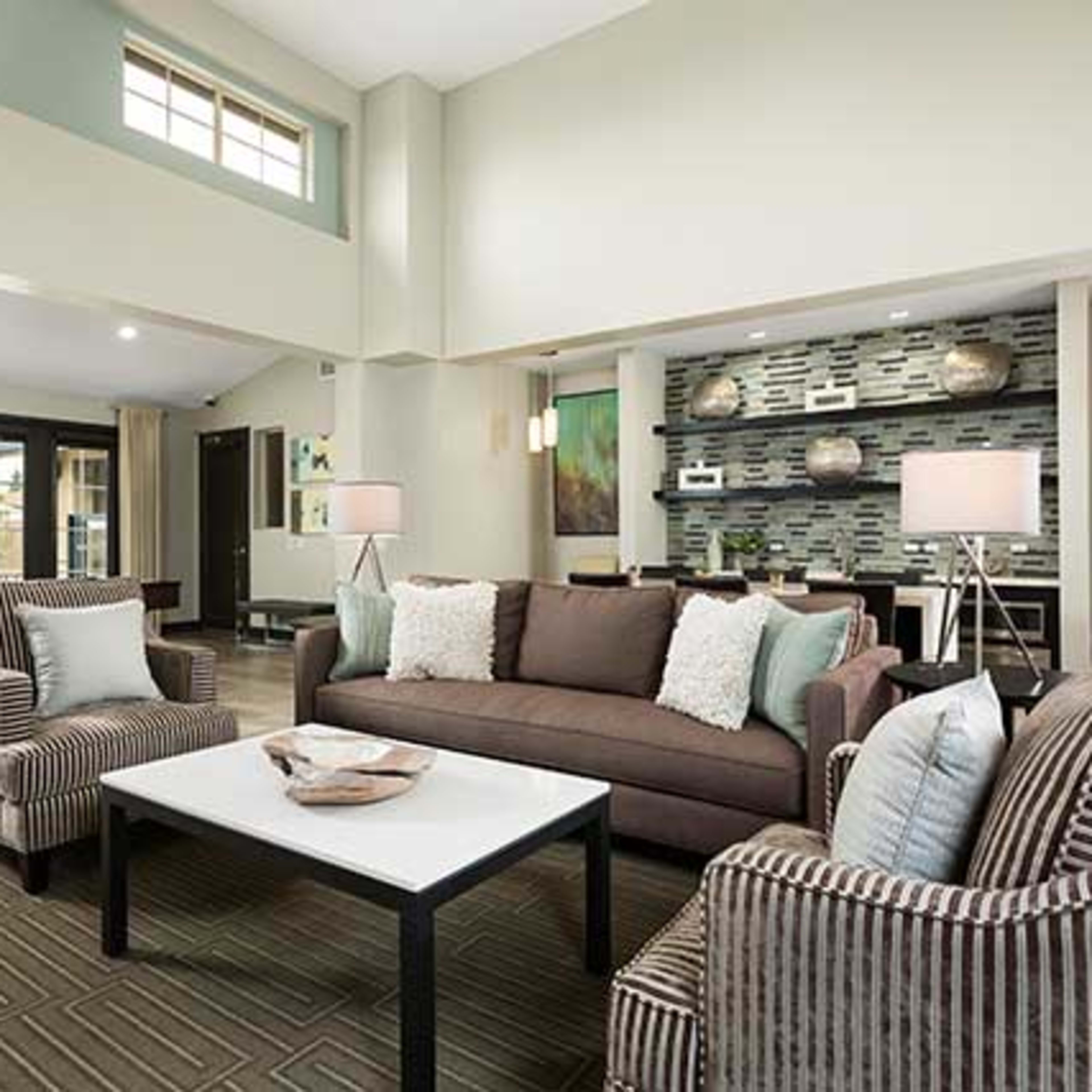 A modern living area featuring a brown sofa, patterned armchairs, a coffee table, and a decorative wall with artwork.