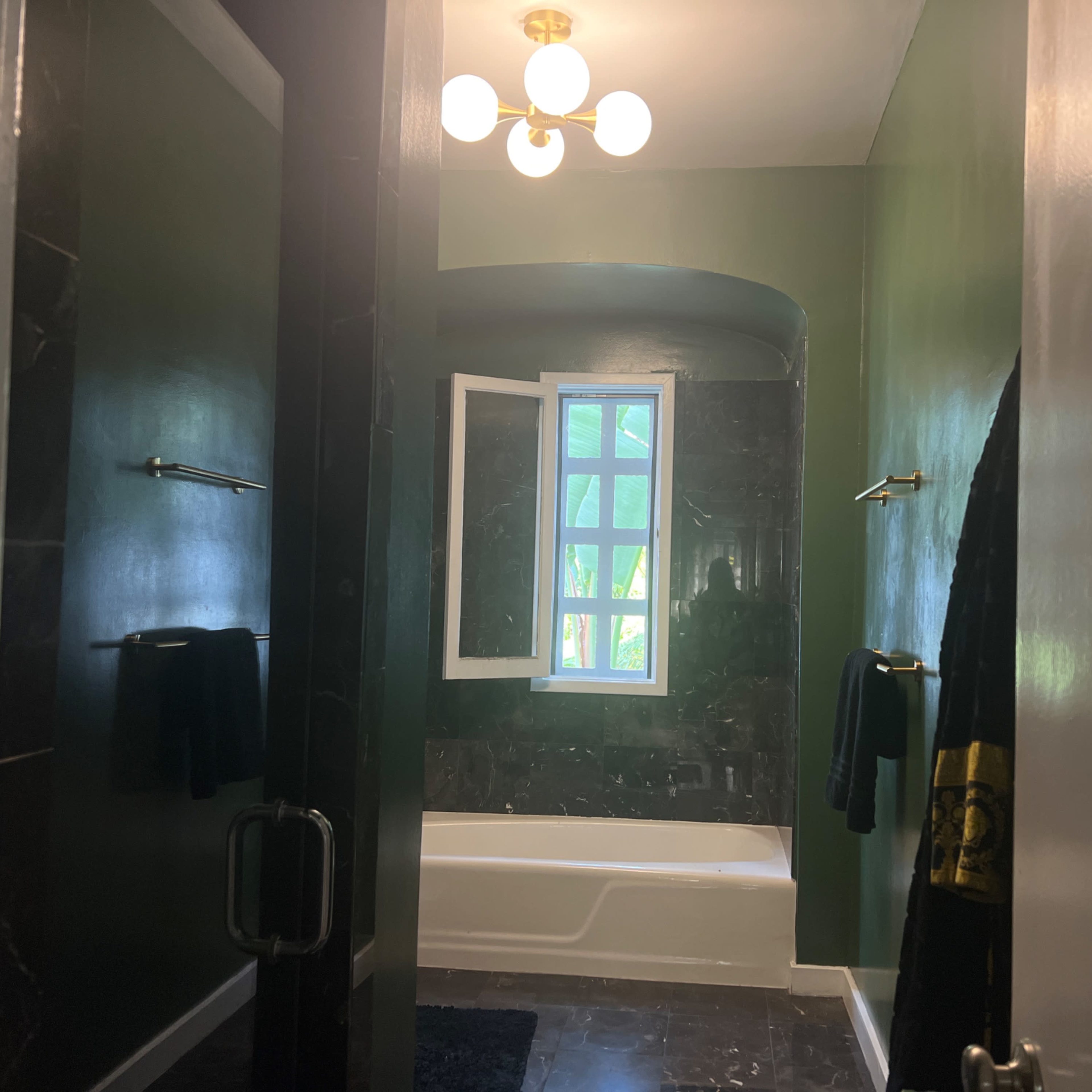 A bathroom with dark green walls, a white bathtub, and a window illuminating the space.