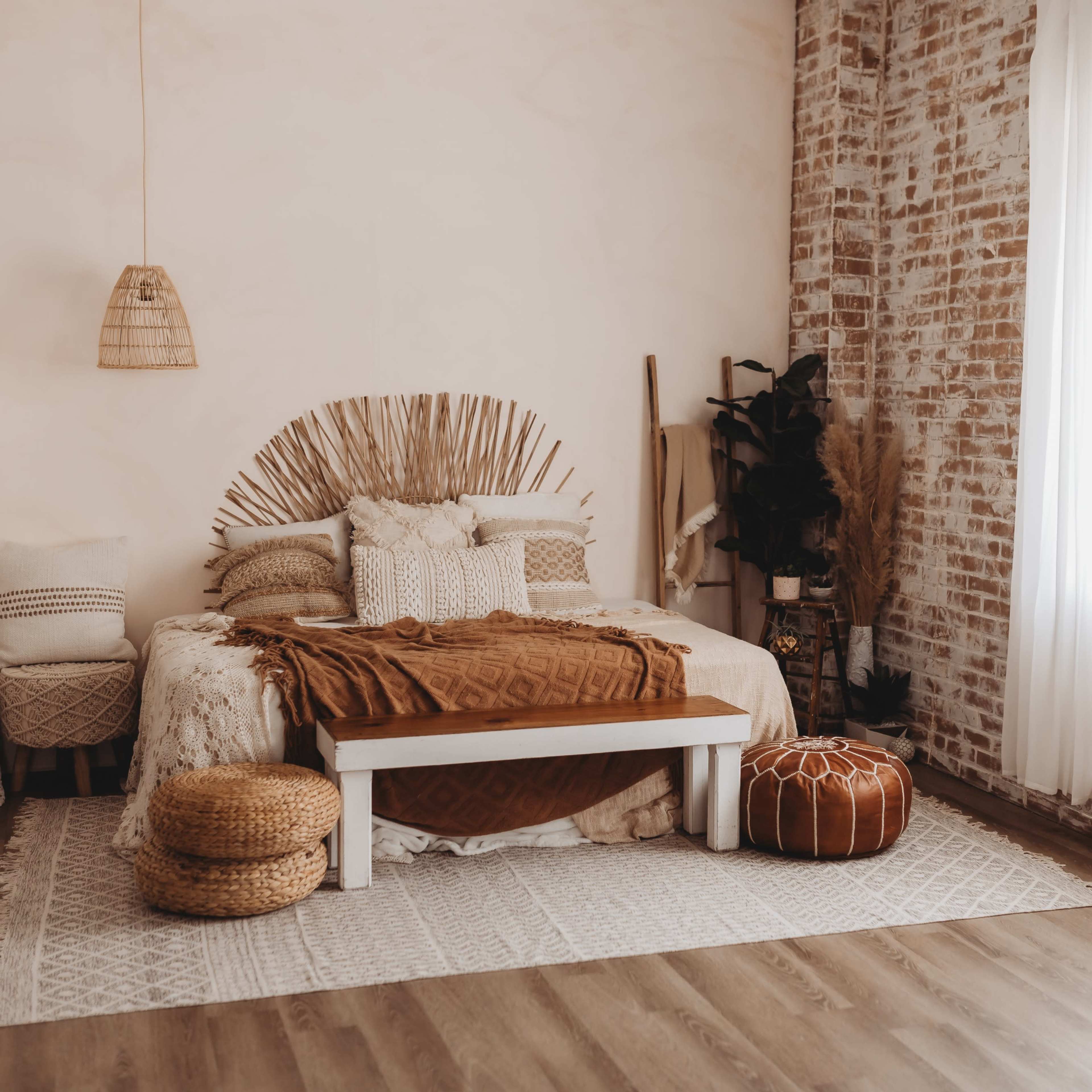 A cozy bedroom featuring a bed with a woven headboard, a large blanket, and natural decor elements, set against a backdrop of exposed brick walls and a bright window.