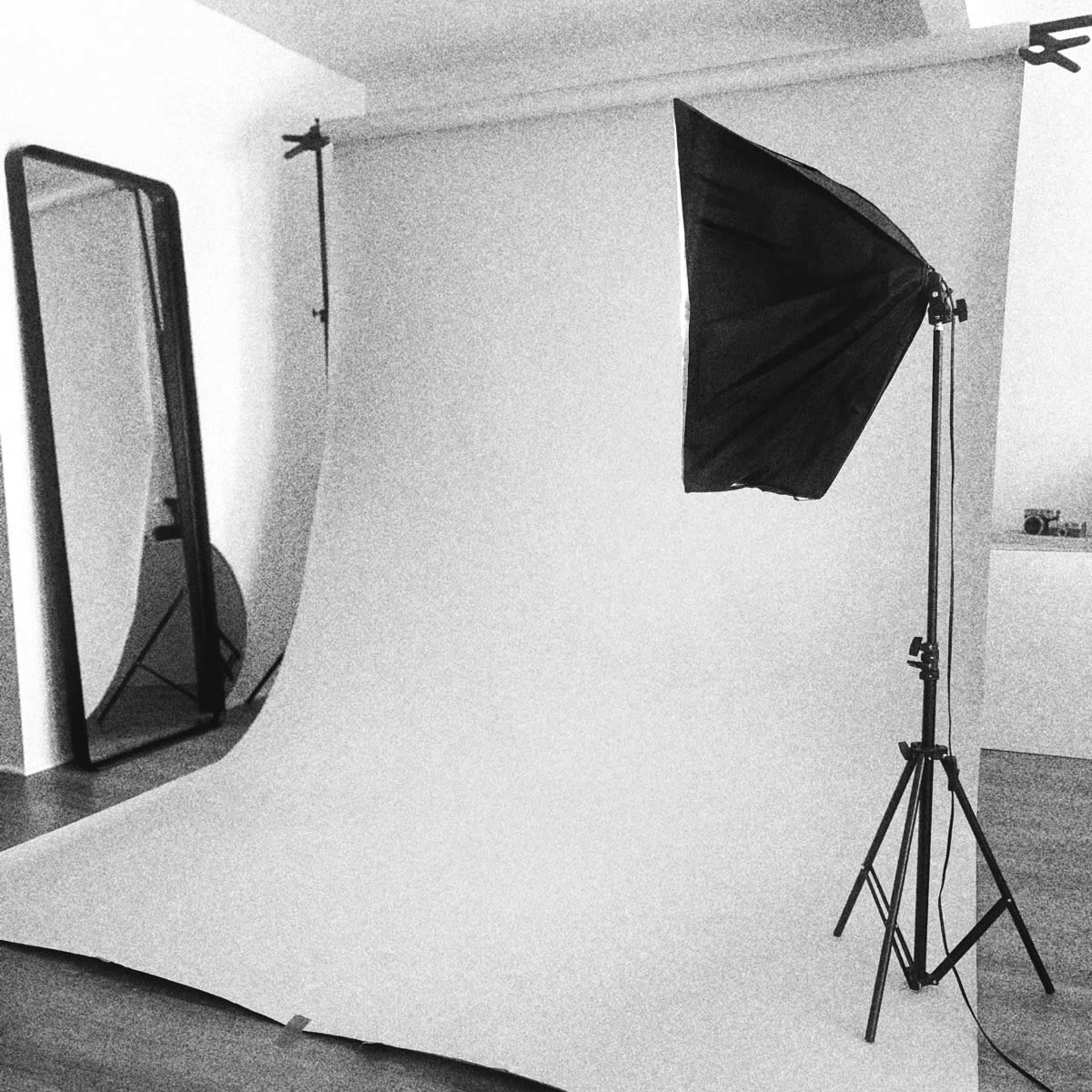 A photography setup with a plain backdrop, a lighting umbrella, and a large mirror in the background.