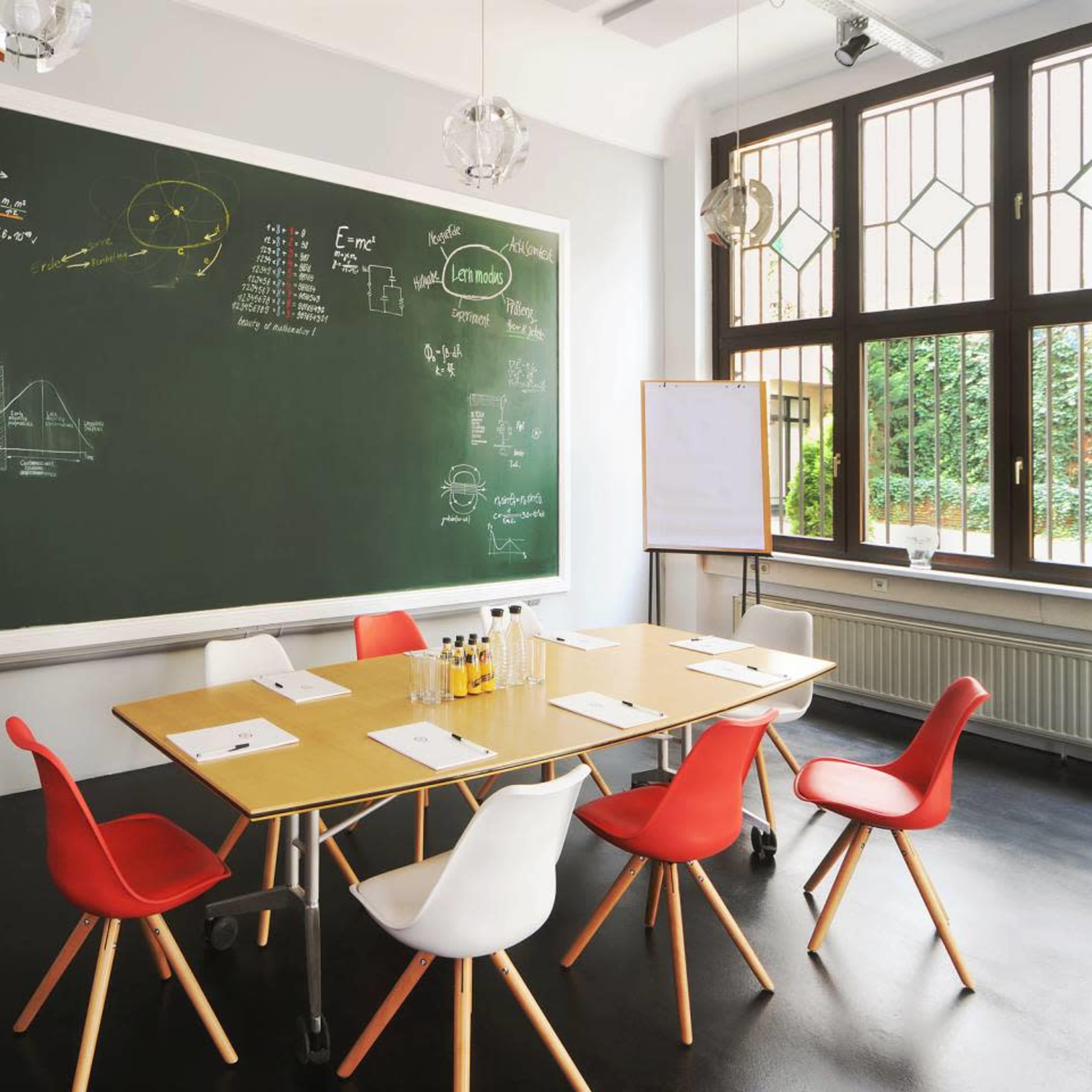 A conference room features a large chalkboard filled with scientific diagrams and equations, surrounded by a wooden table and colorful chairs.