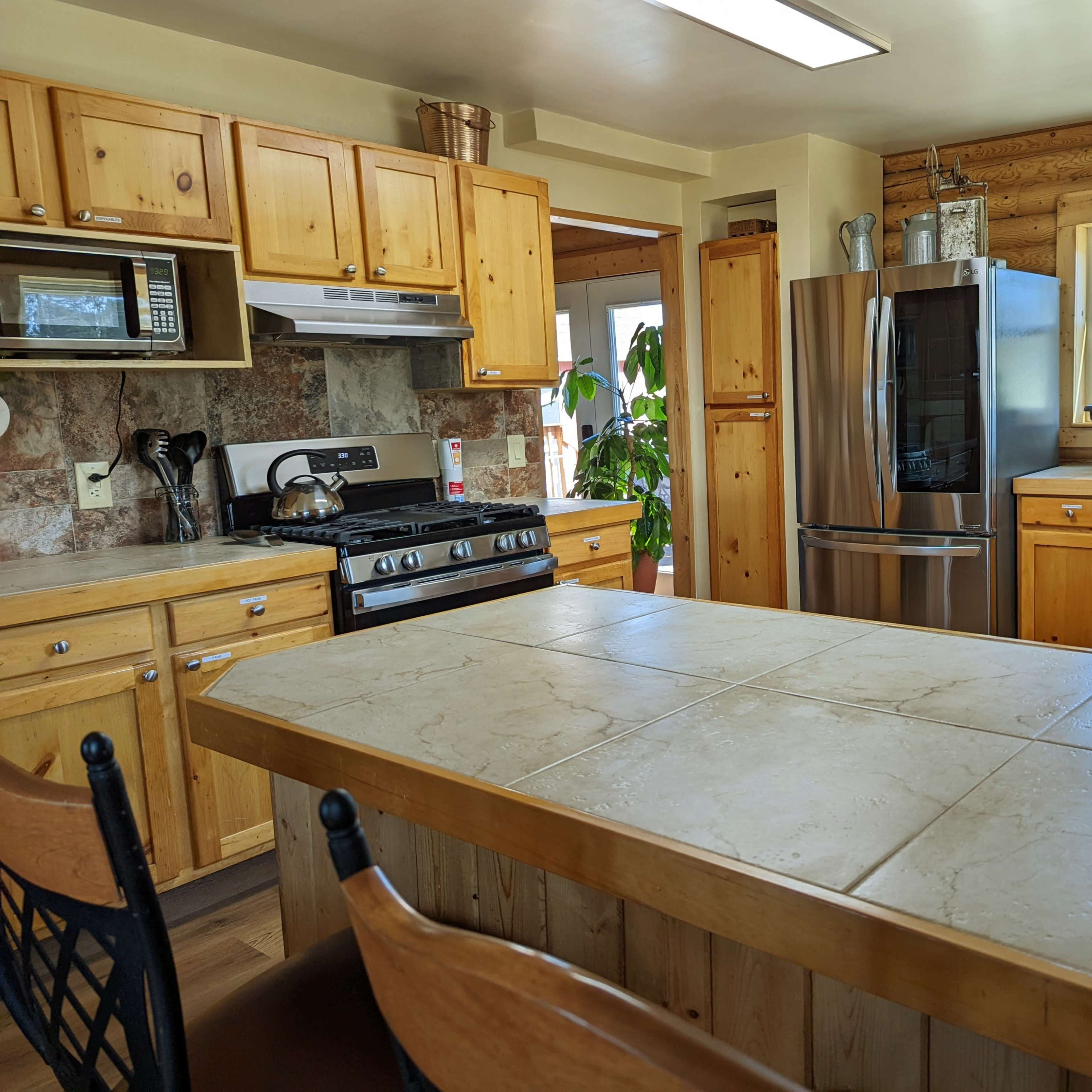 The kitchen features wooden cabinetry, a gas stove, a modern refrigerator, and a large island with a tiled countertop.