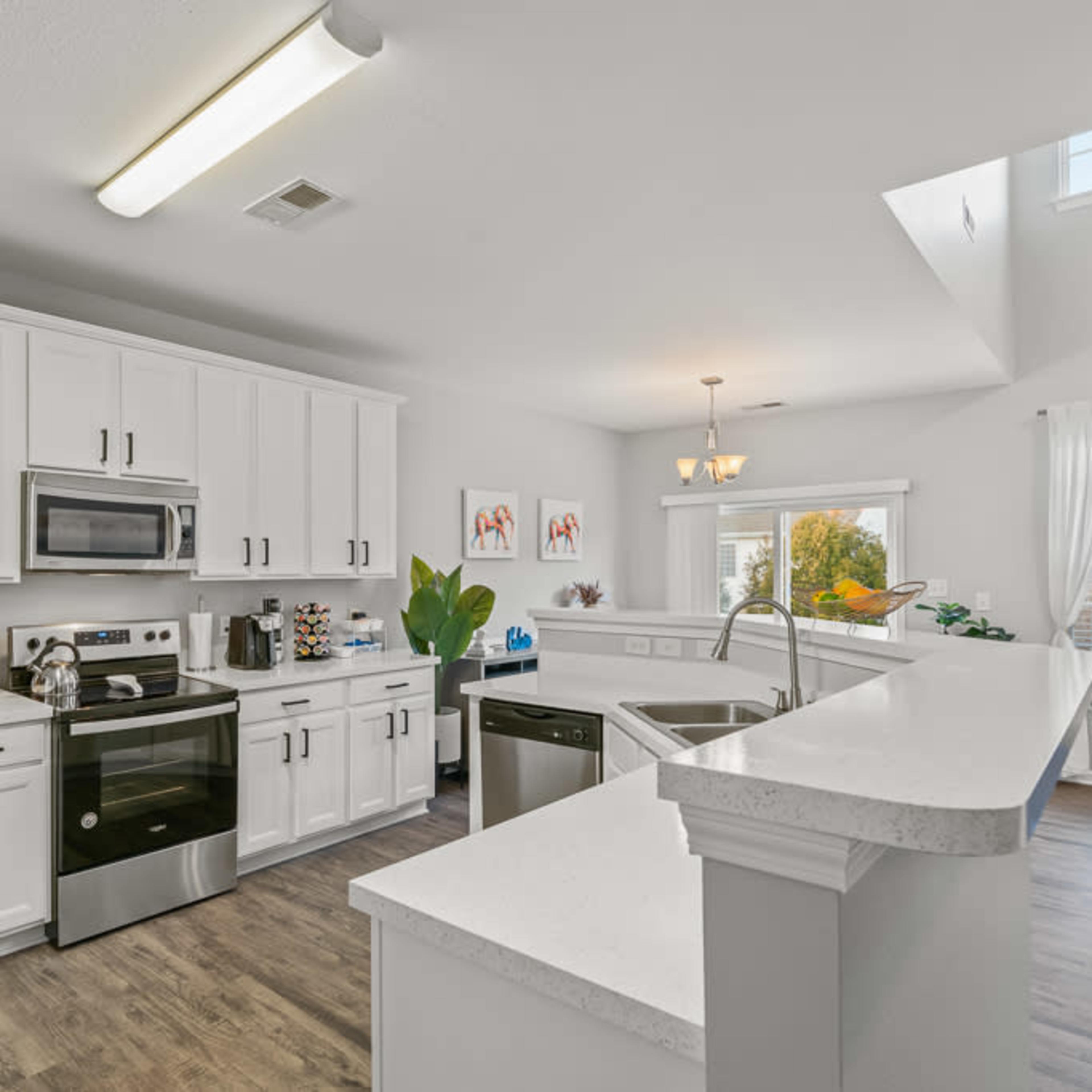 A modern kitchen features white cabinets, stainless steel appliances, and a spacious layout with natural light streaming in through a window.