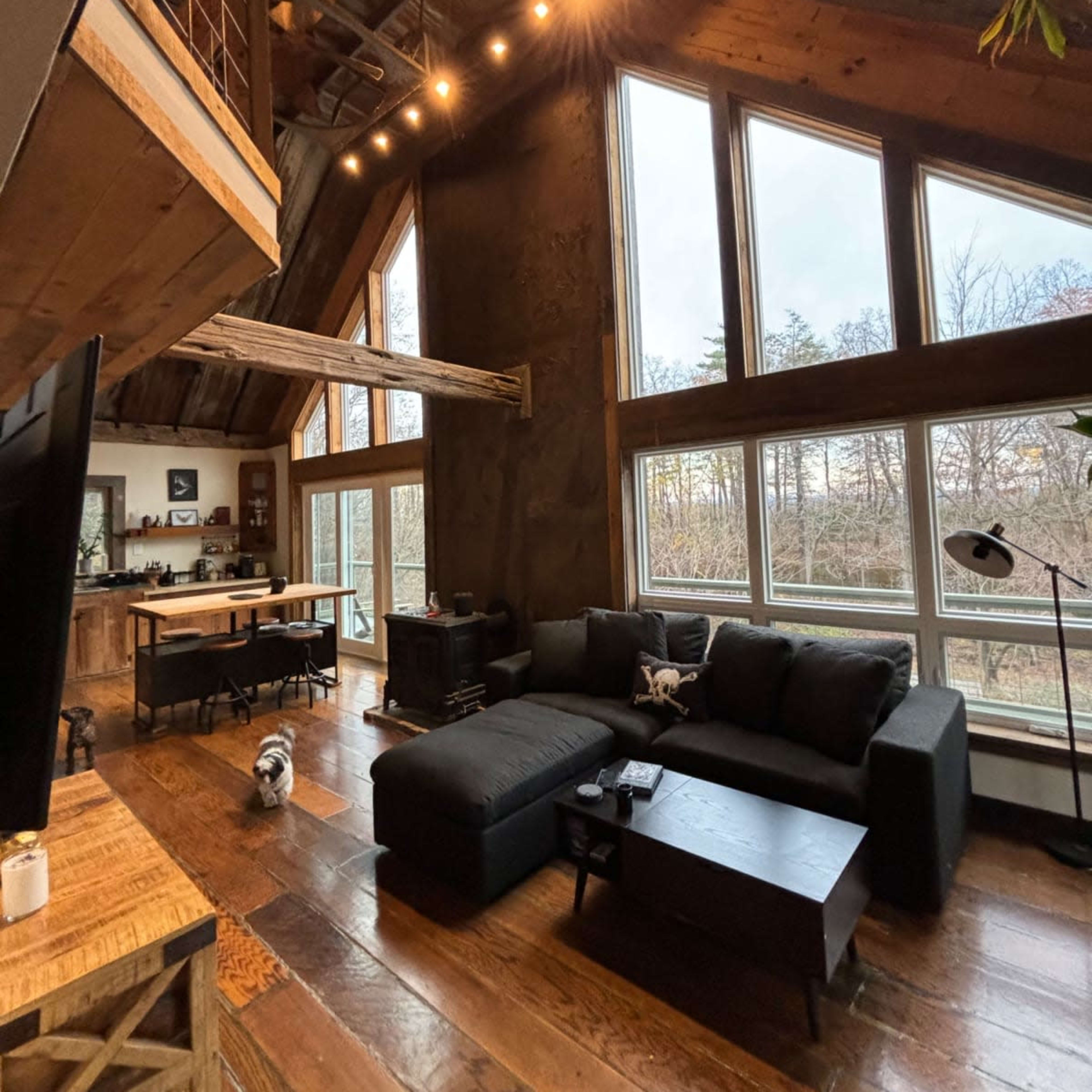 A spacious, modern living area features a black sectional sofa, a wooden coffee table, large windows, and a lofted space above.