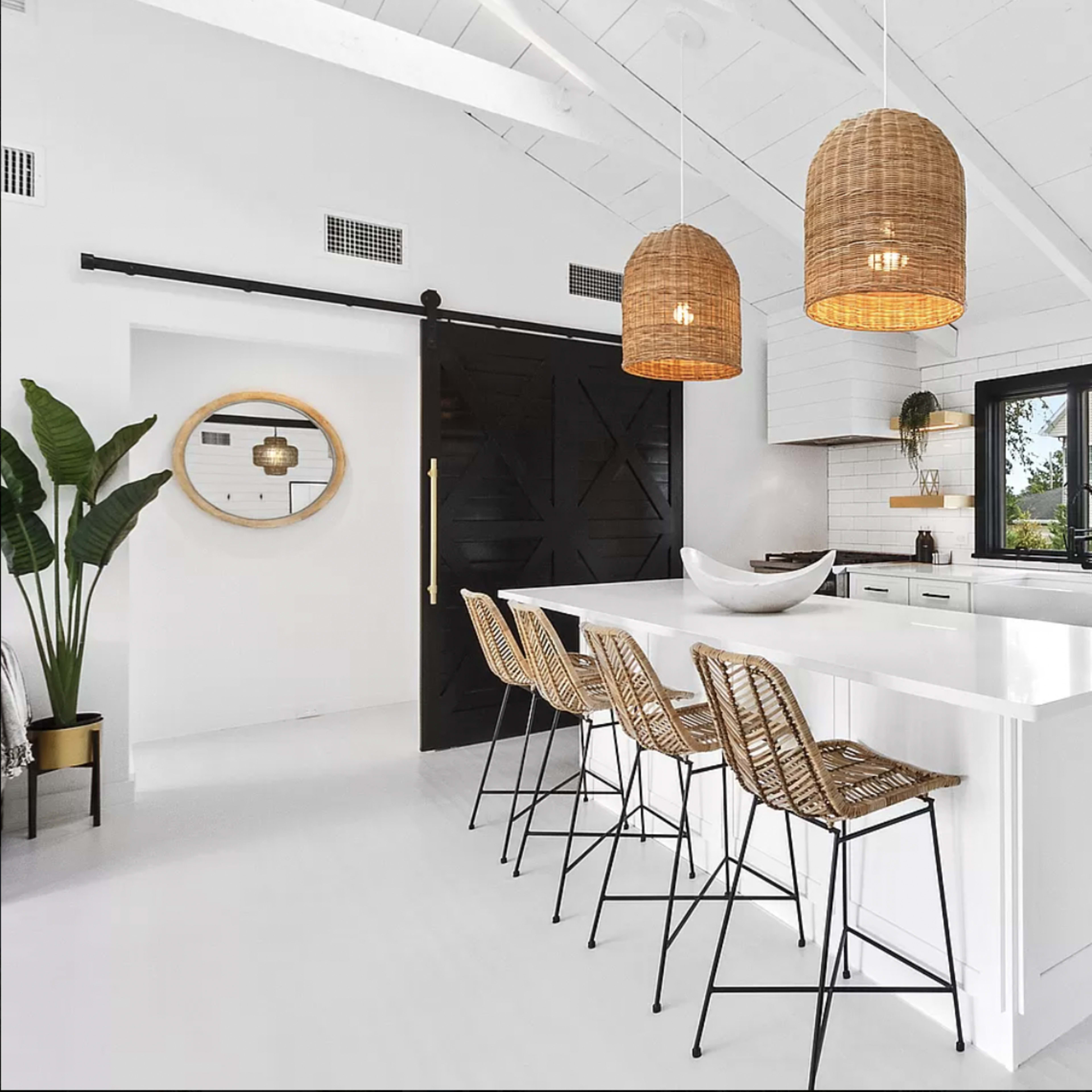 A modern kitchen features a white island with bar stools, pendant lighting, stainless steel appliances, and a sliding barn door.