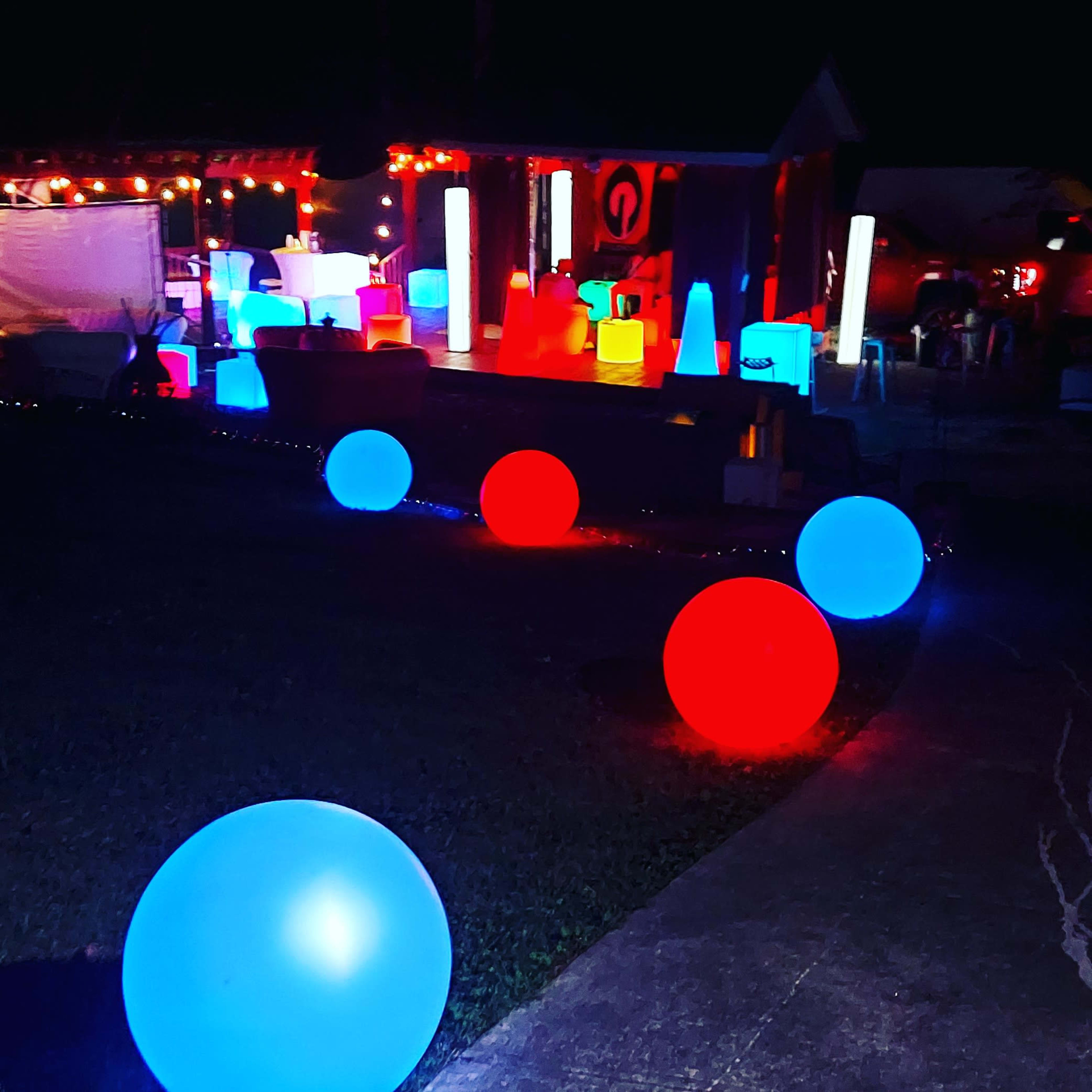 The scene features a decorative outdoor area illuminated by various colorful, glowing orbs and shapes, with blue and red lights highlighting a pathway and surrounding structures.