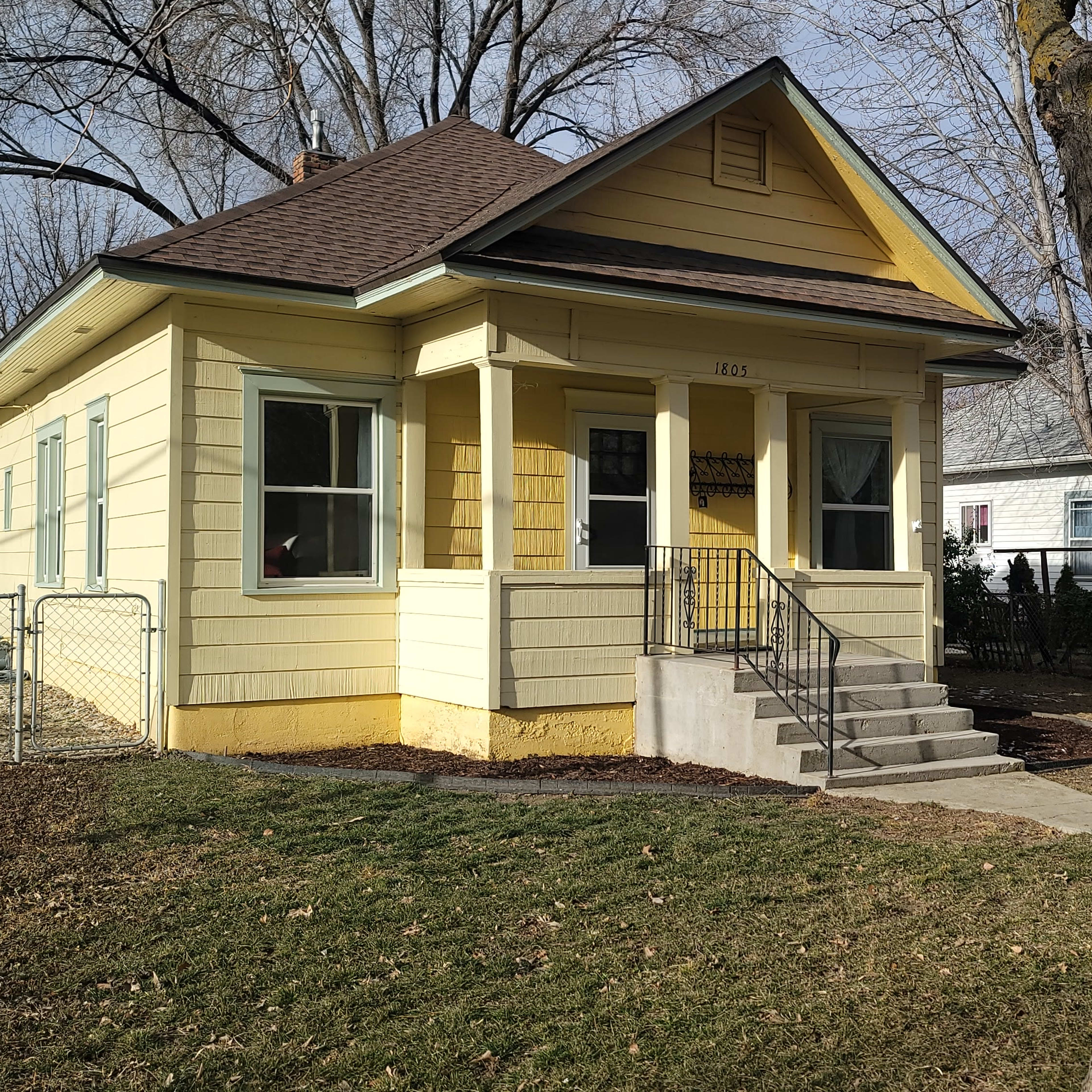 A yellow house with a porch and steps surrounded by trees and a lawn.