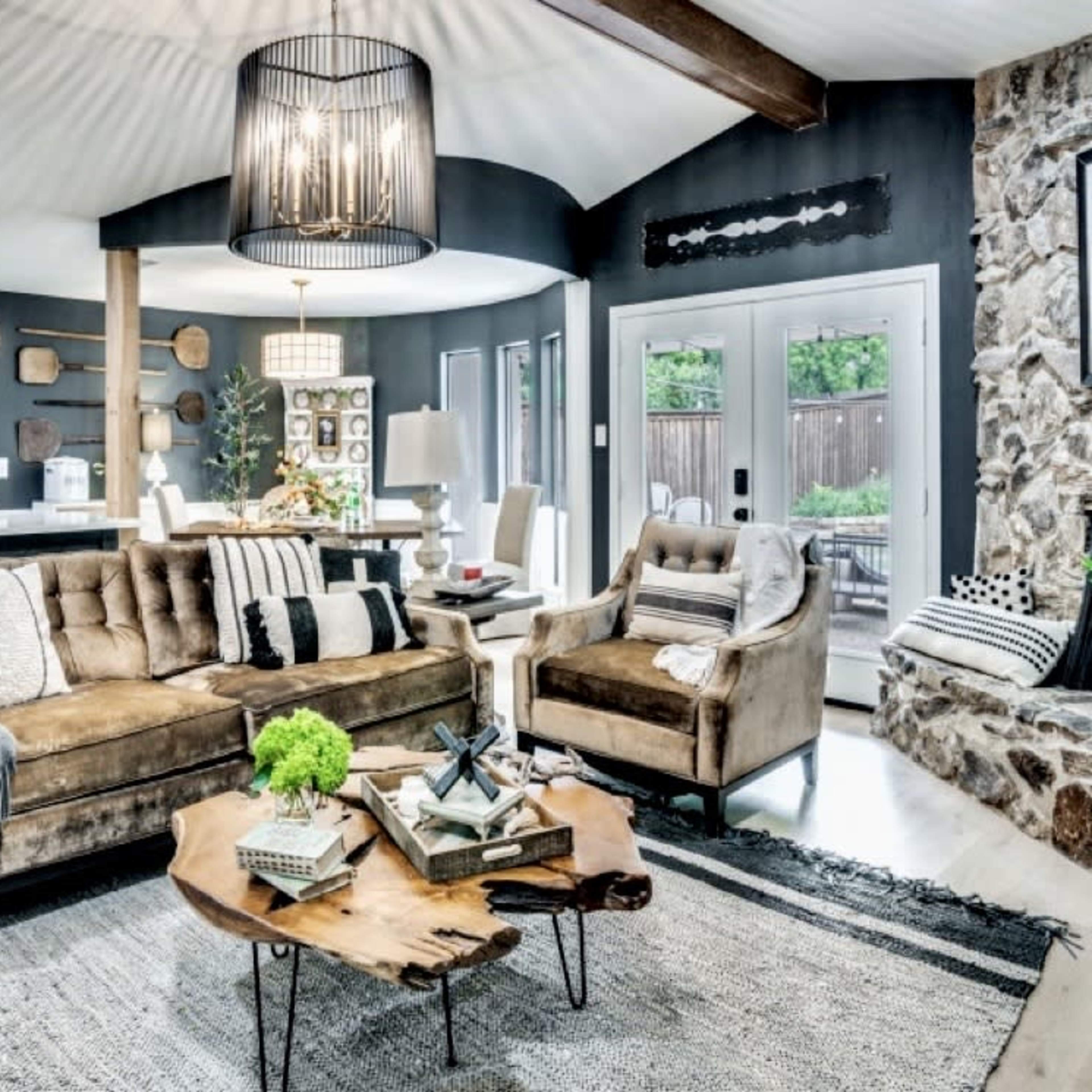 A modern living room features a plush brown sofa and armchair, a wooden coffee table, and a stone accent wall, with an open kitchen visible in the background.