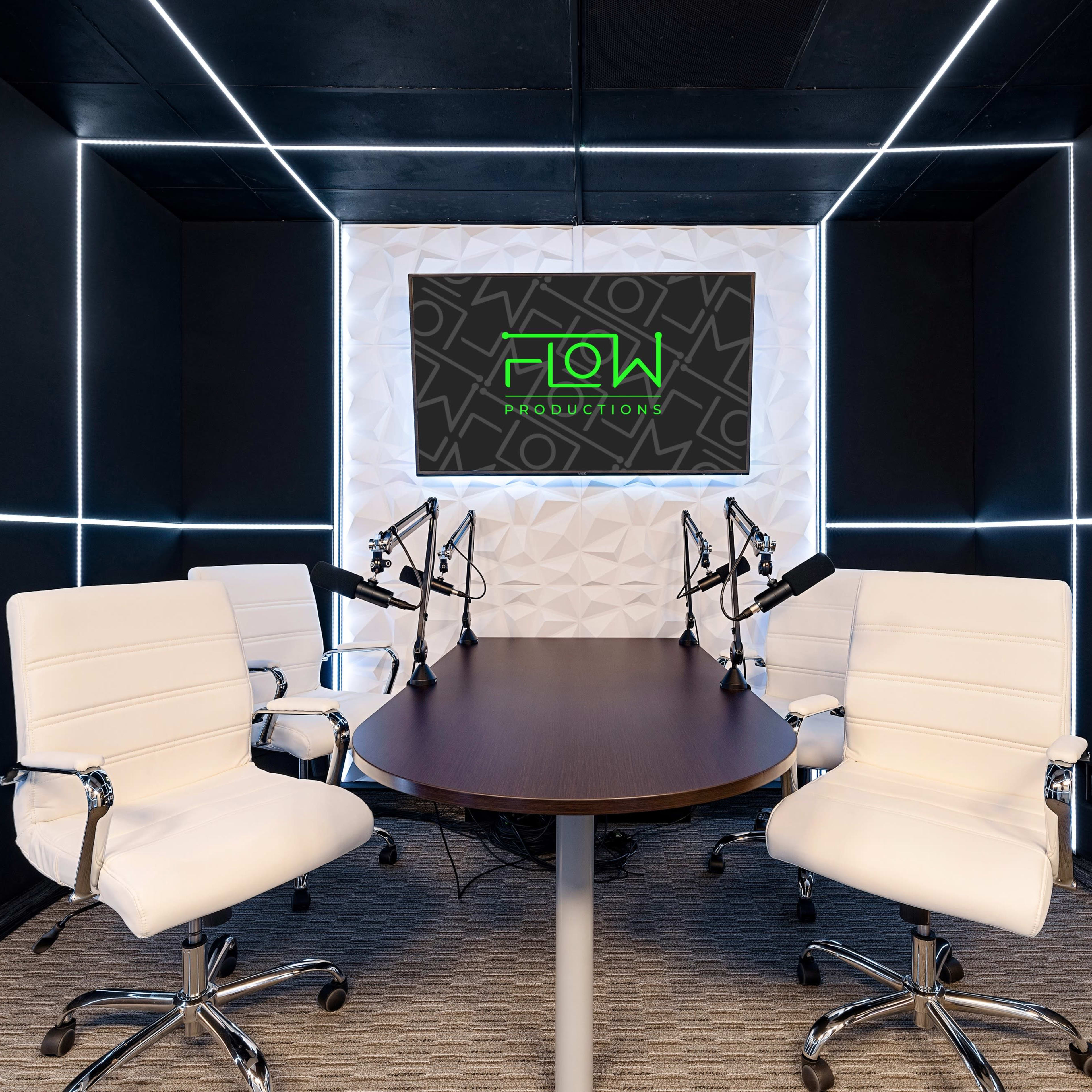 A modern recording studio with a round table, four white chairs, and two microphones positioned at the center, framed by illuminated geometric panels.