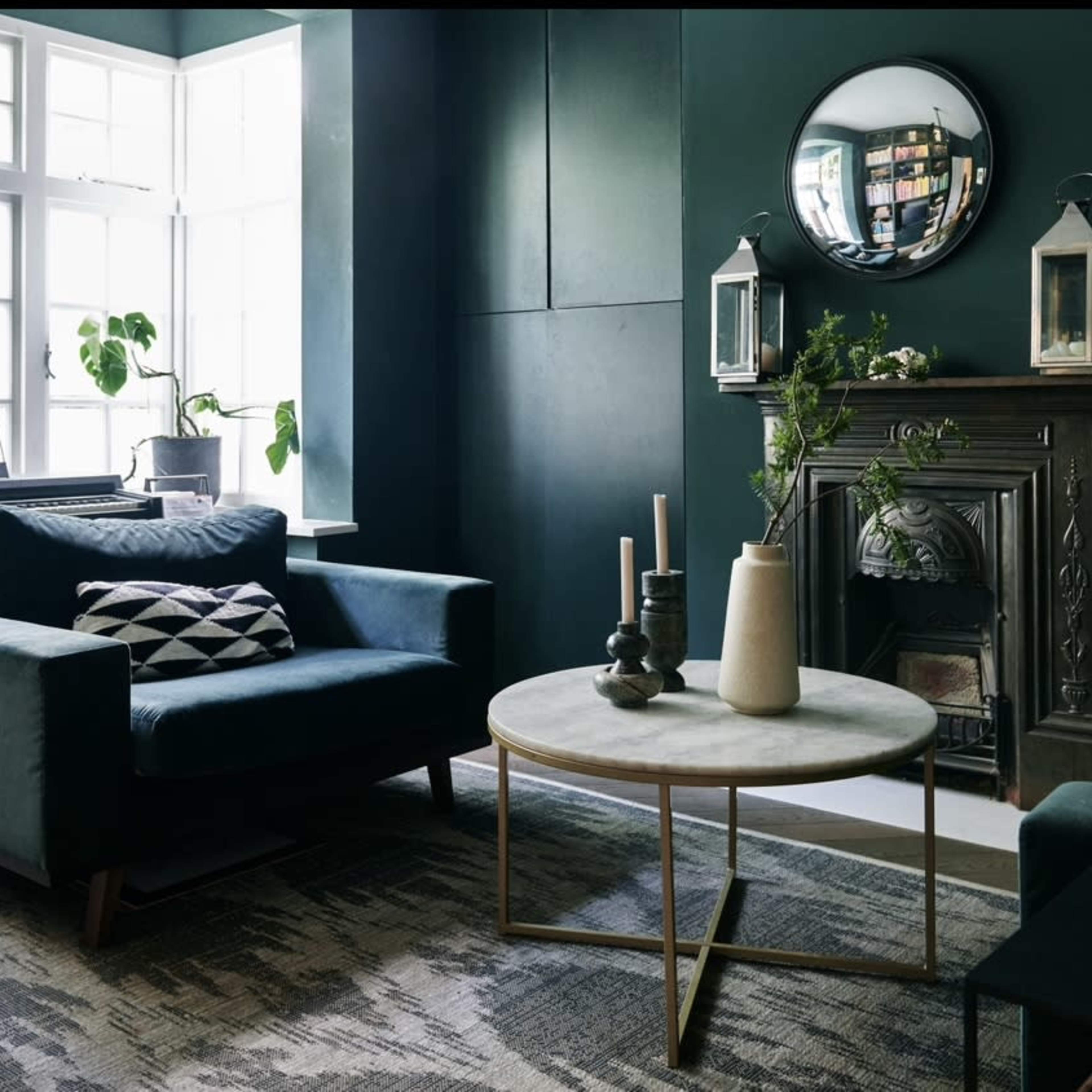 A living room with dark green walls, two modern sofas, a round coffee table, and a decorative fireplace.