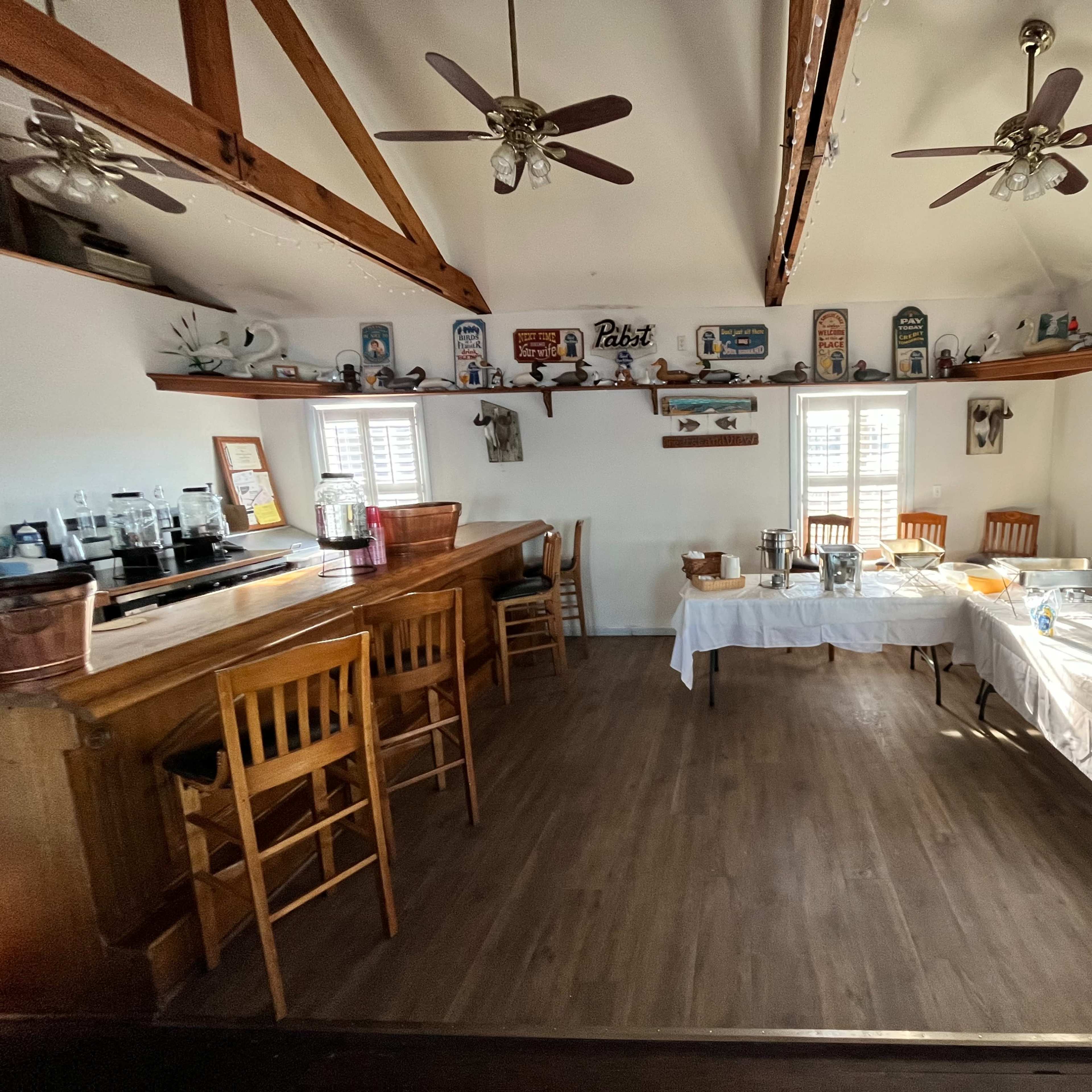A table setup with chairs, a wooden bar area, and shelves displaying decor in a room with a light-colored interior.