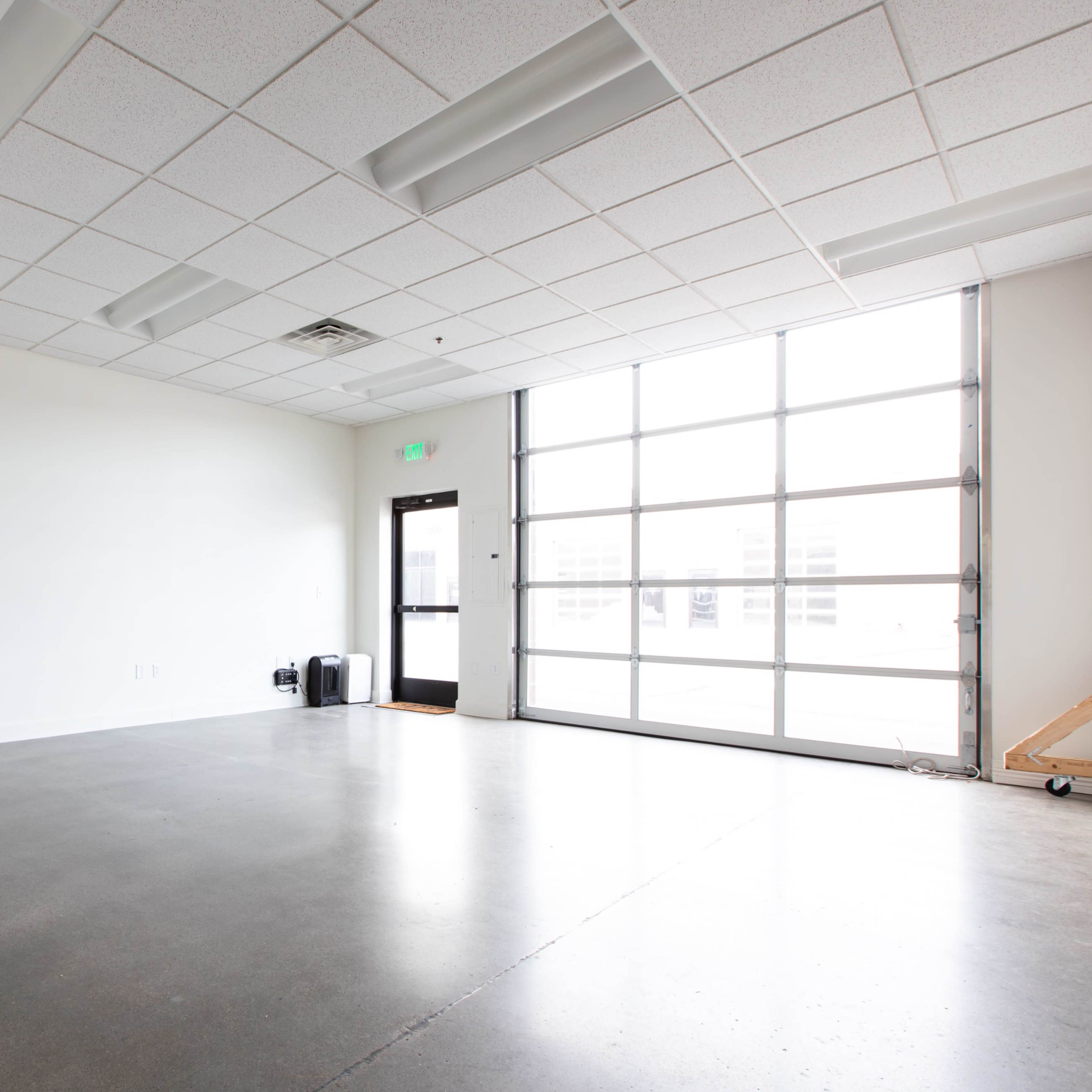 An empty room with a concrete floor, a large window, and a door leading outside.