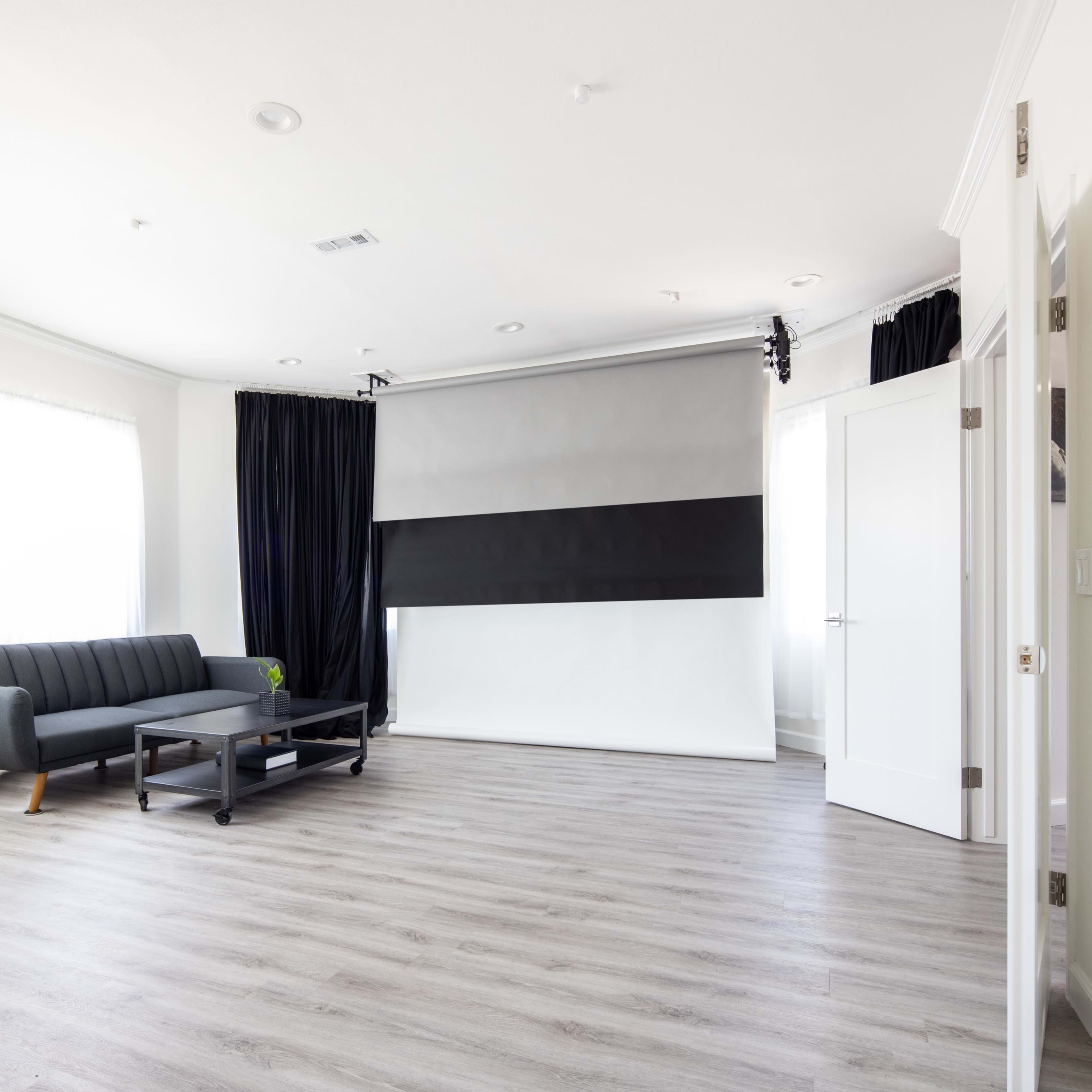 A modern, minimalist room featuring a gray sofa, a black coffee table, and a large projection screen set against a light-colored wall.