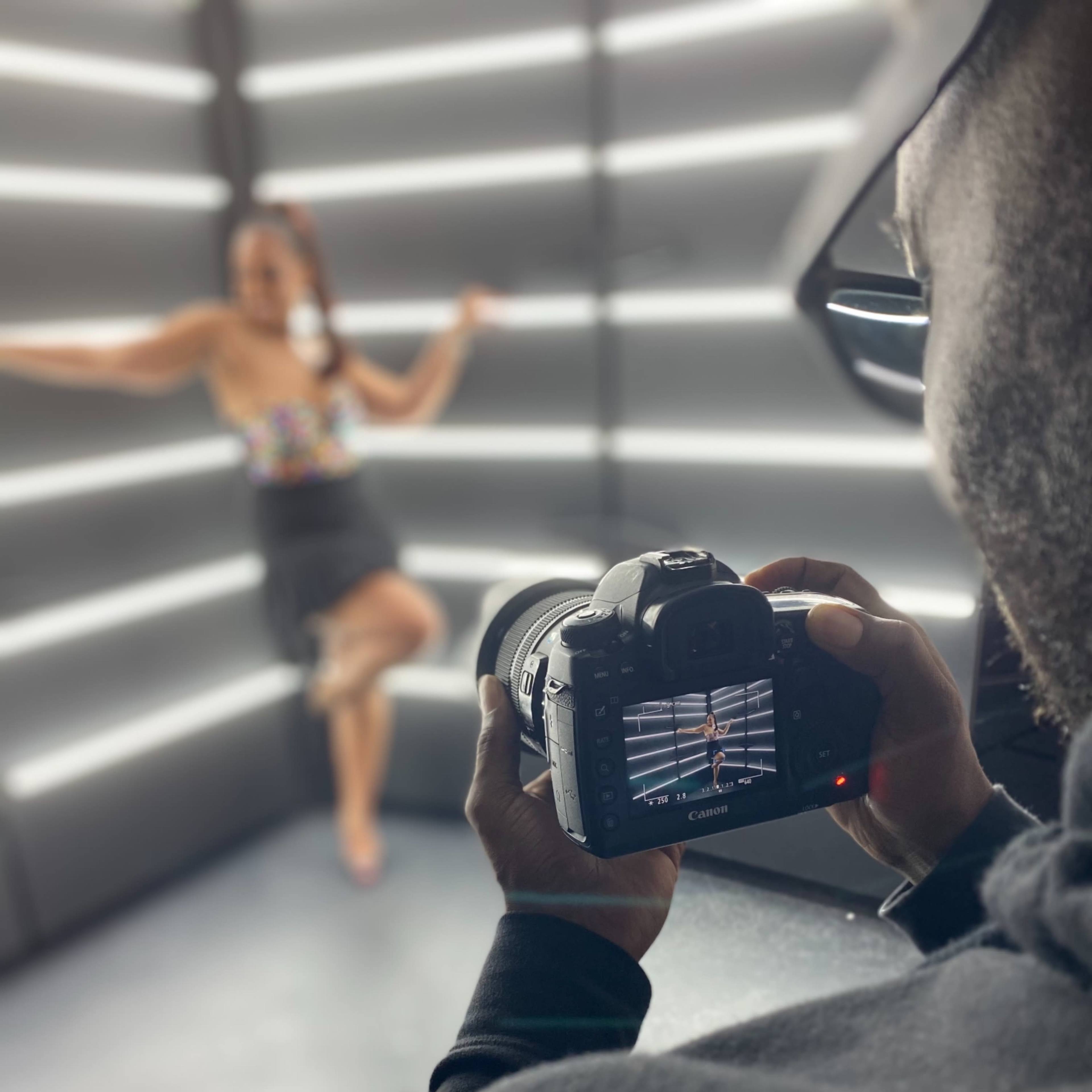 A photographer captures a model posing against illuminated vertical lines in a studio setting.