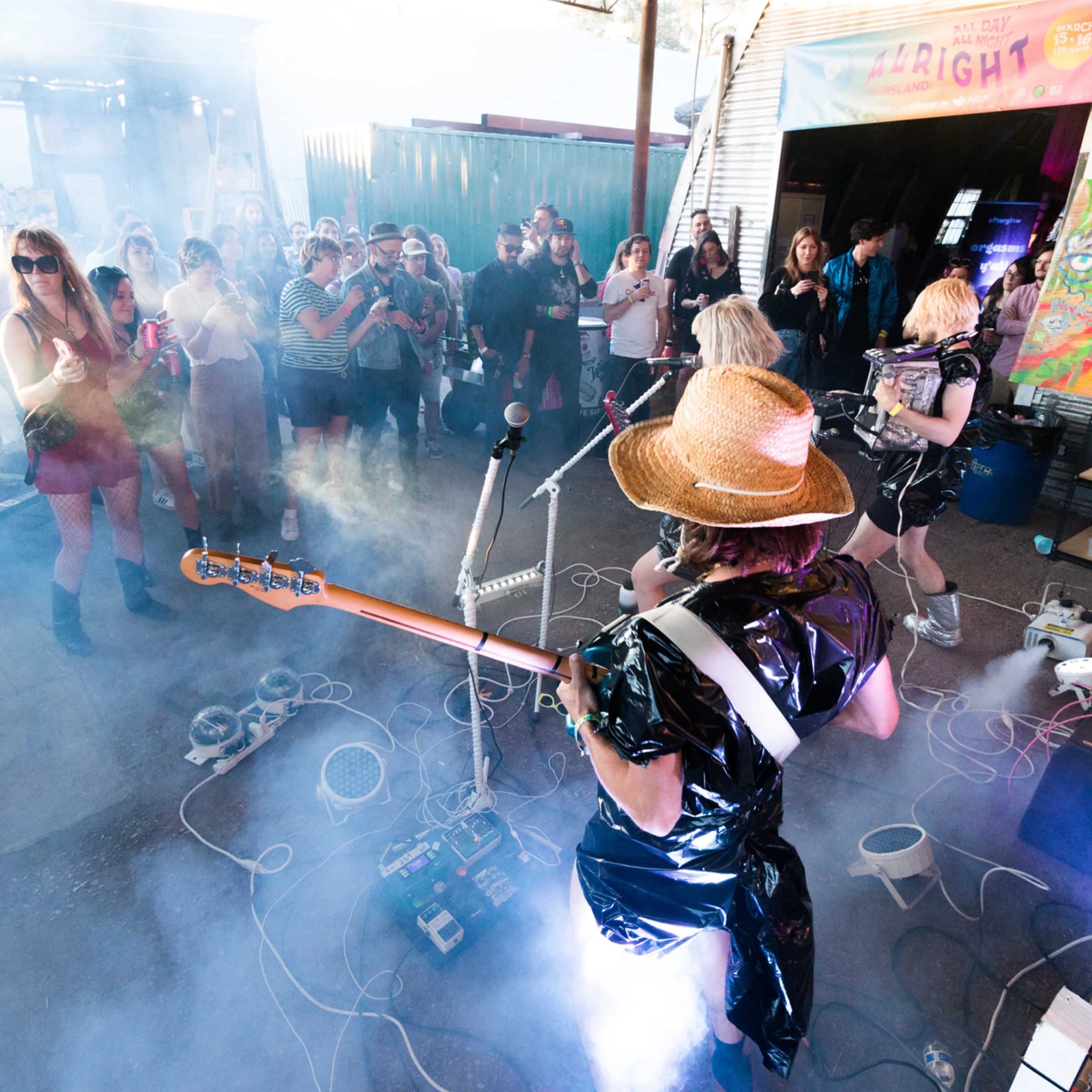 A group of musicians performs on stage surrounded by fog, while an audience watches enthusiastically.