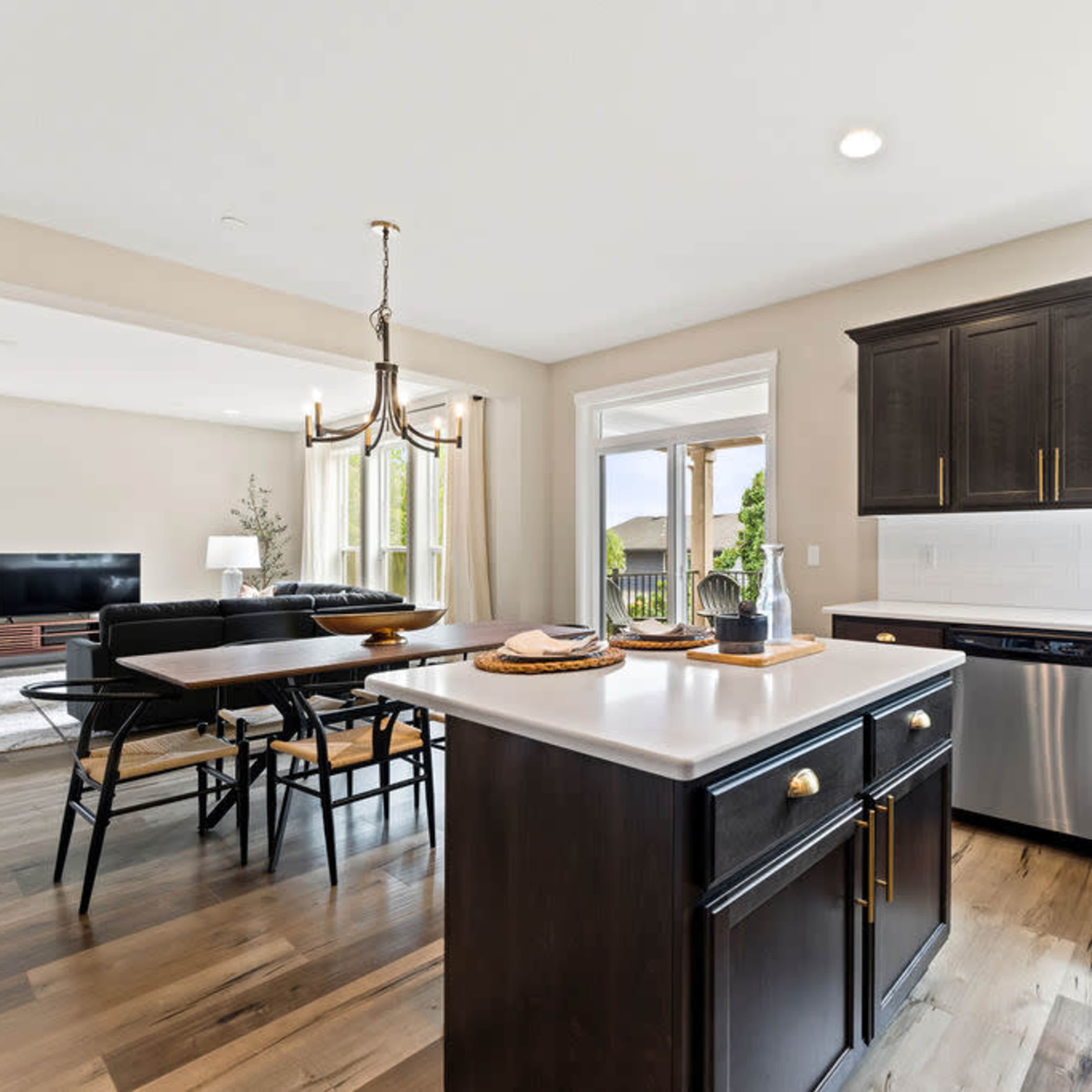 A modern kitchen with dark cabinetry, a white countertop, and large windows that provide natural light.