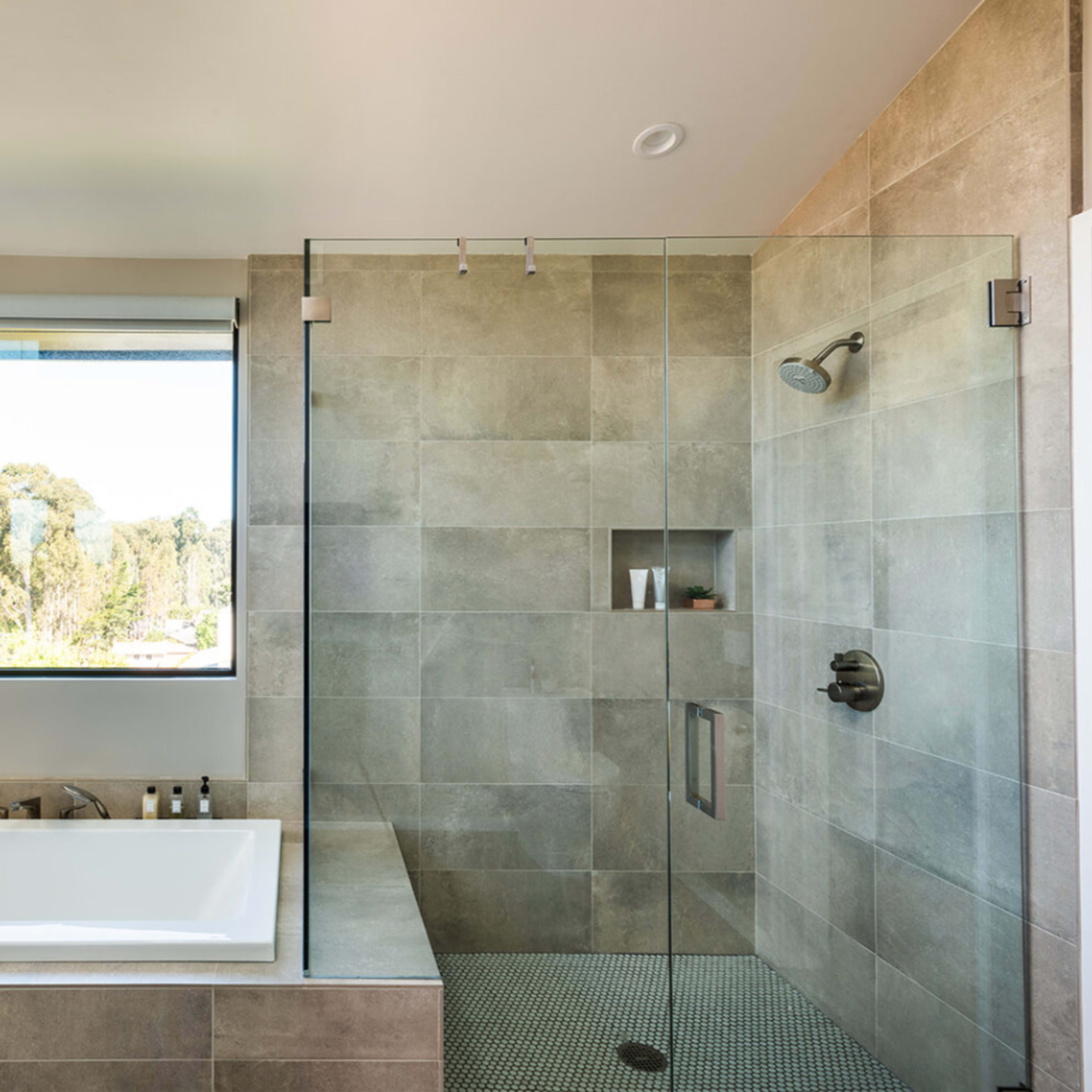 A modern bathroom featuring a glass-enclosed shower, a freestanding bathtub, and a large window overlooking greenery.