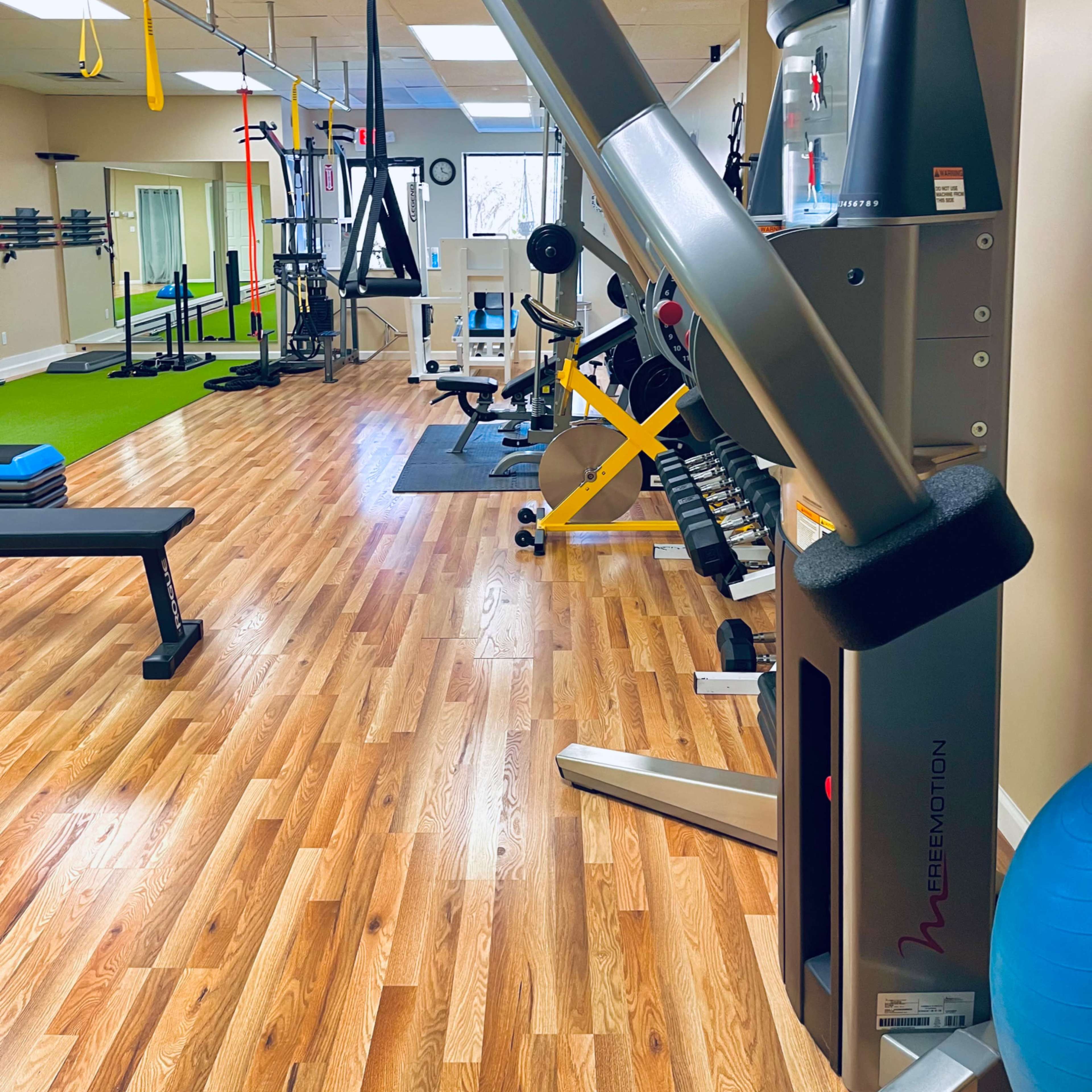A well-equipped gym interior featuring various exercise machines, weights, and training equipment on wooden flooring.