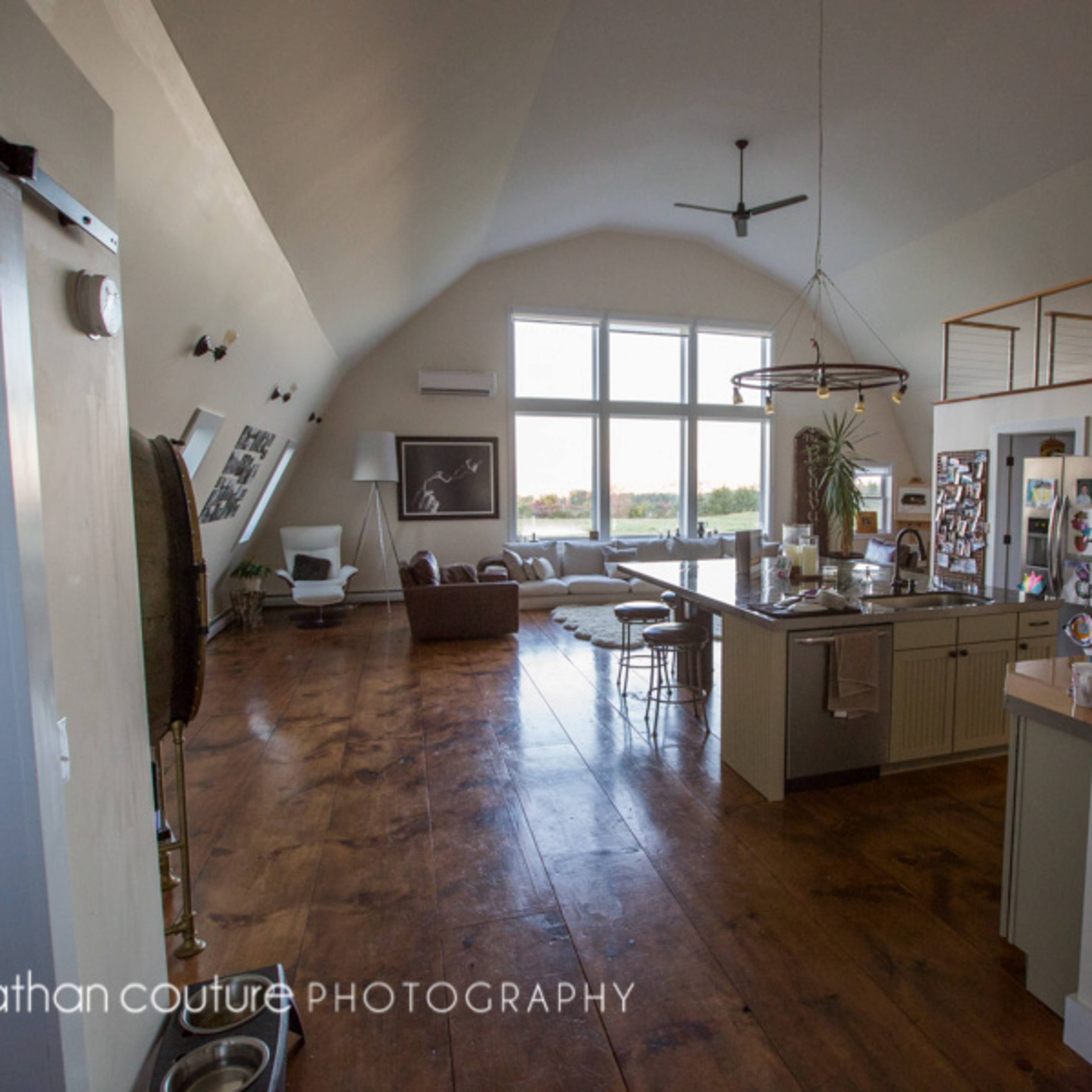 A spacious, modern living area with large windows, a kitchen island, and a seating area featuring a couch and armchairs.
