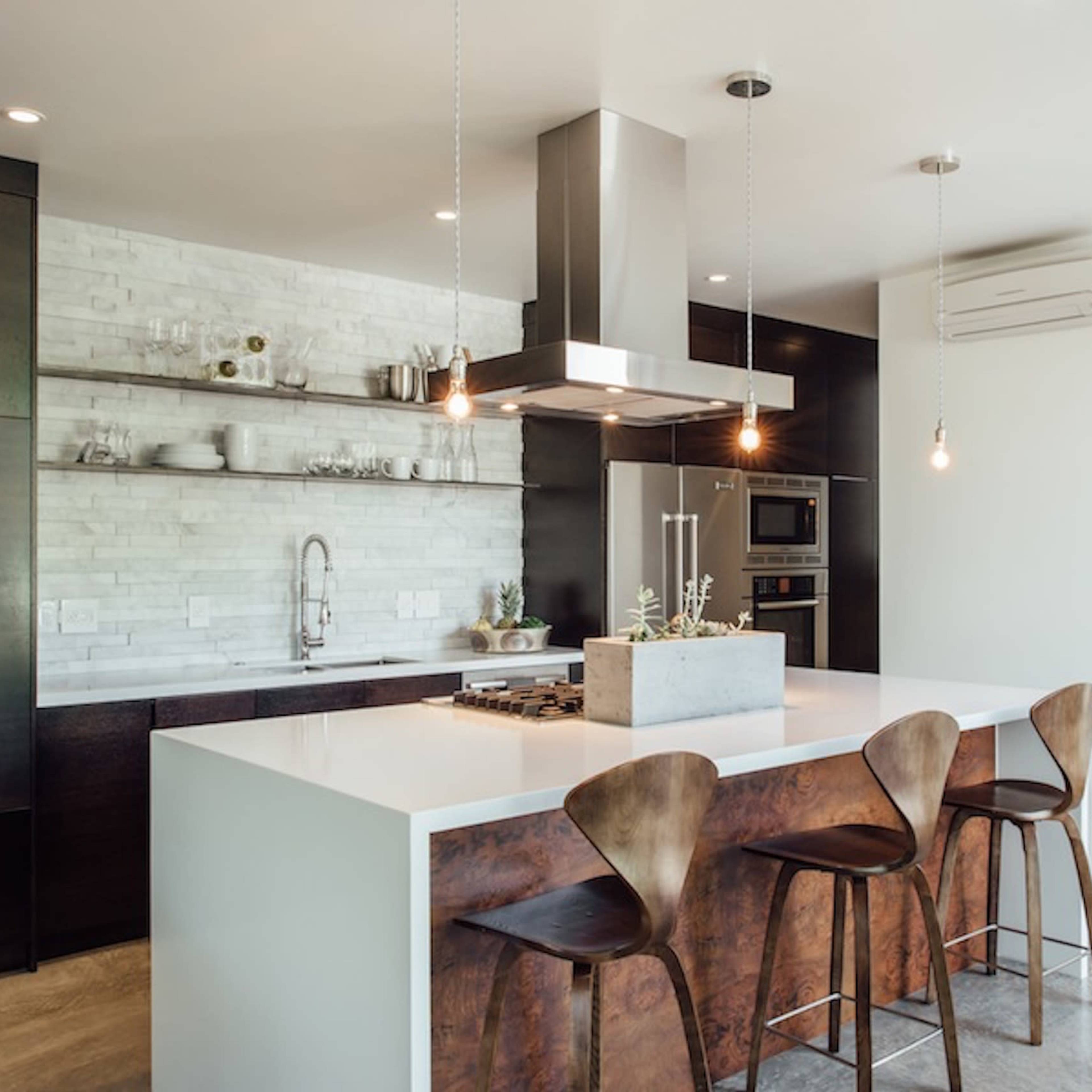 A modern kitchen featuring a central island with four wooden stools, a stainless steel range hood, and a minimalist design.