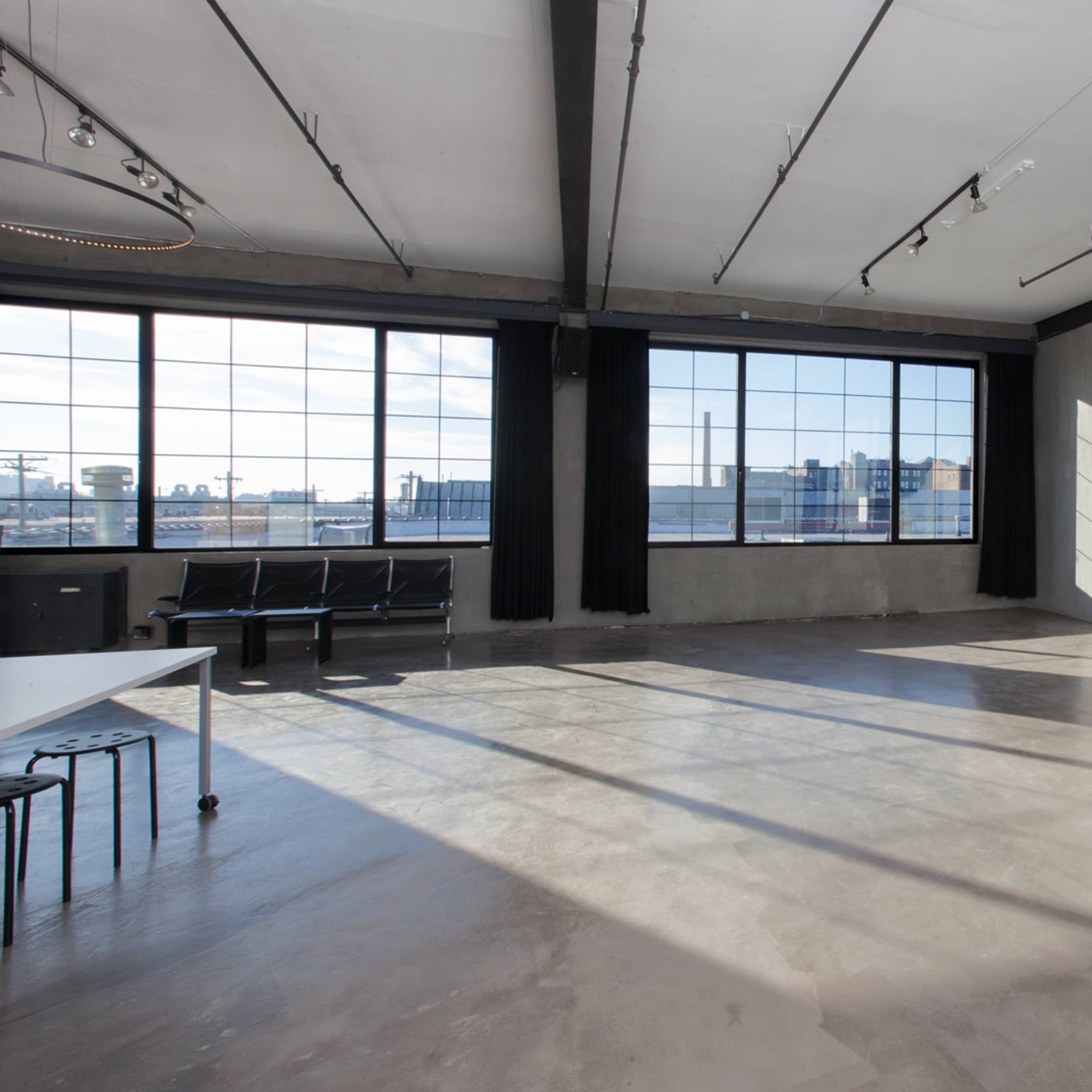 An empty industrial-style room with large windows, concrete flooring, and minimal furnishings.