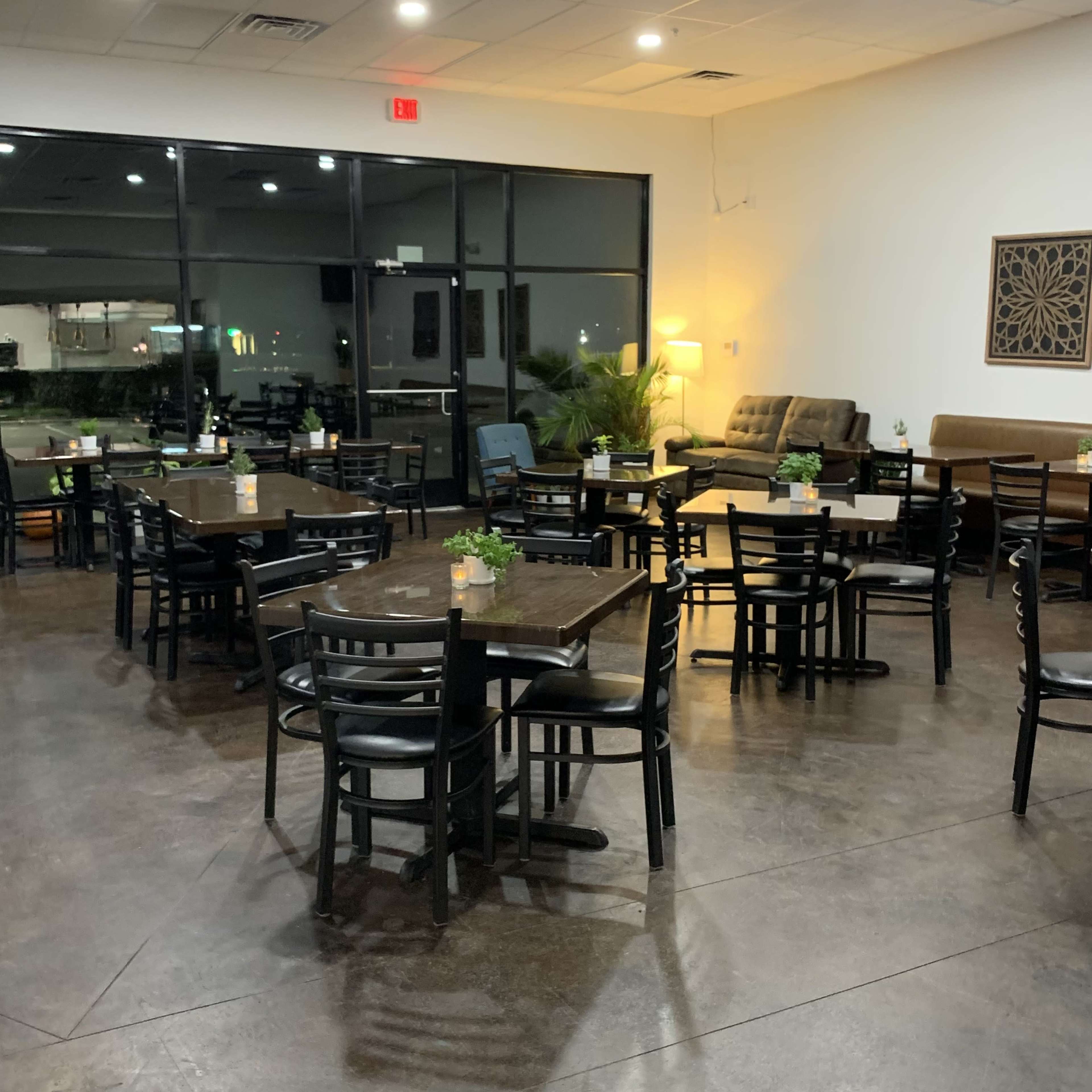 A spacious restaurant interior with several unoccupied tables arranged neatly and a seating area with a couch in the background.