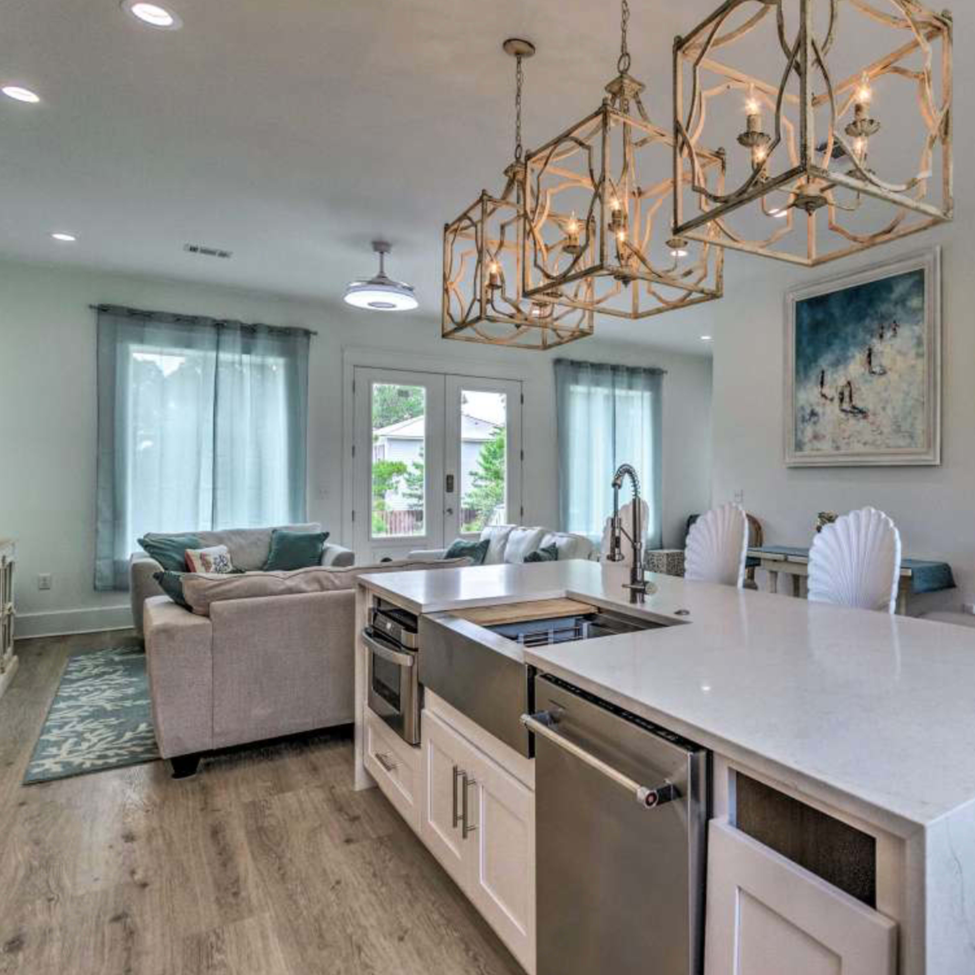 A modern kitchen with a large island featuring bar seating, pendant lights above, and an open layout connecting to a living area.