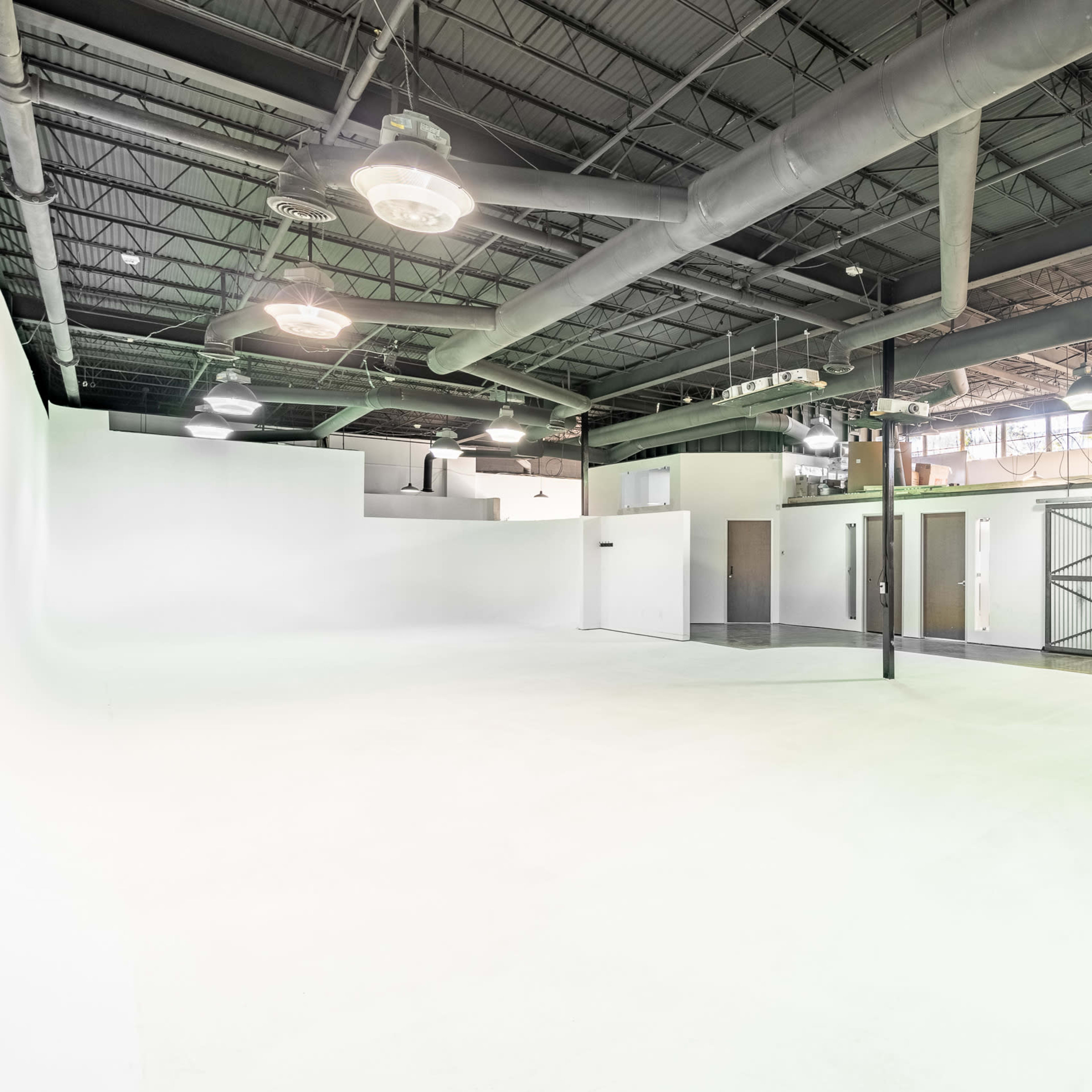 A spacious, empty studio with white walls, high ceilings, and several doors leading to other areas.