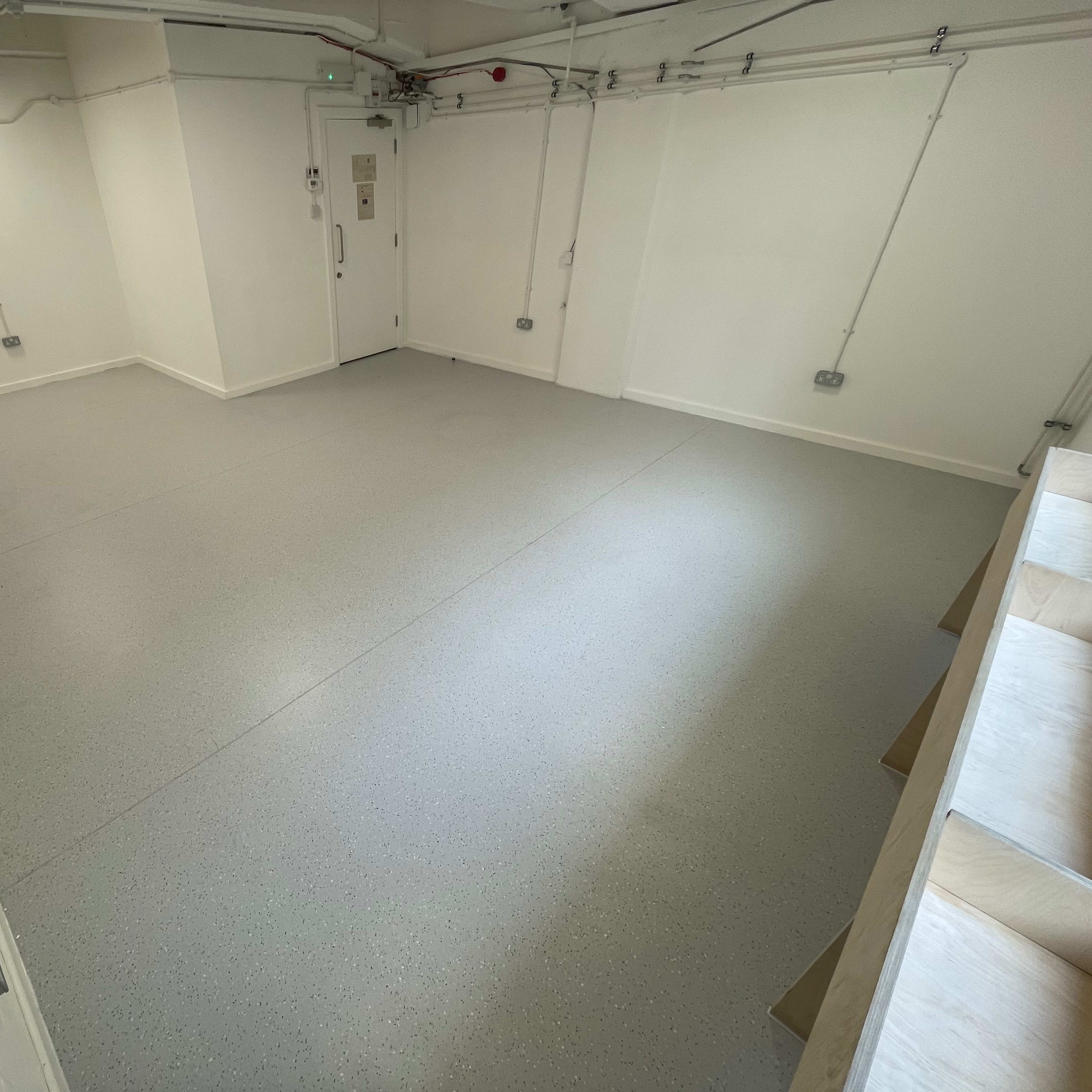 An empty room with gray flooring, white walls, and a door on one side.