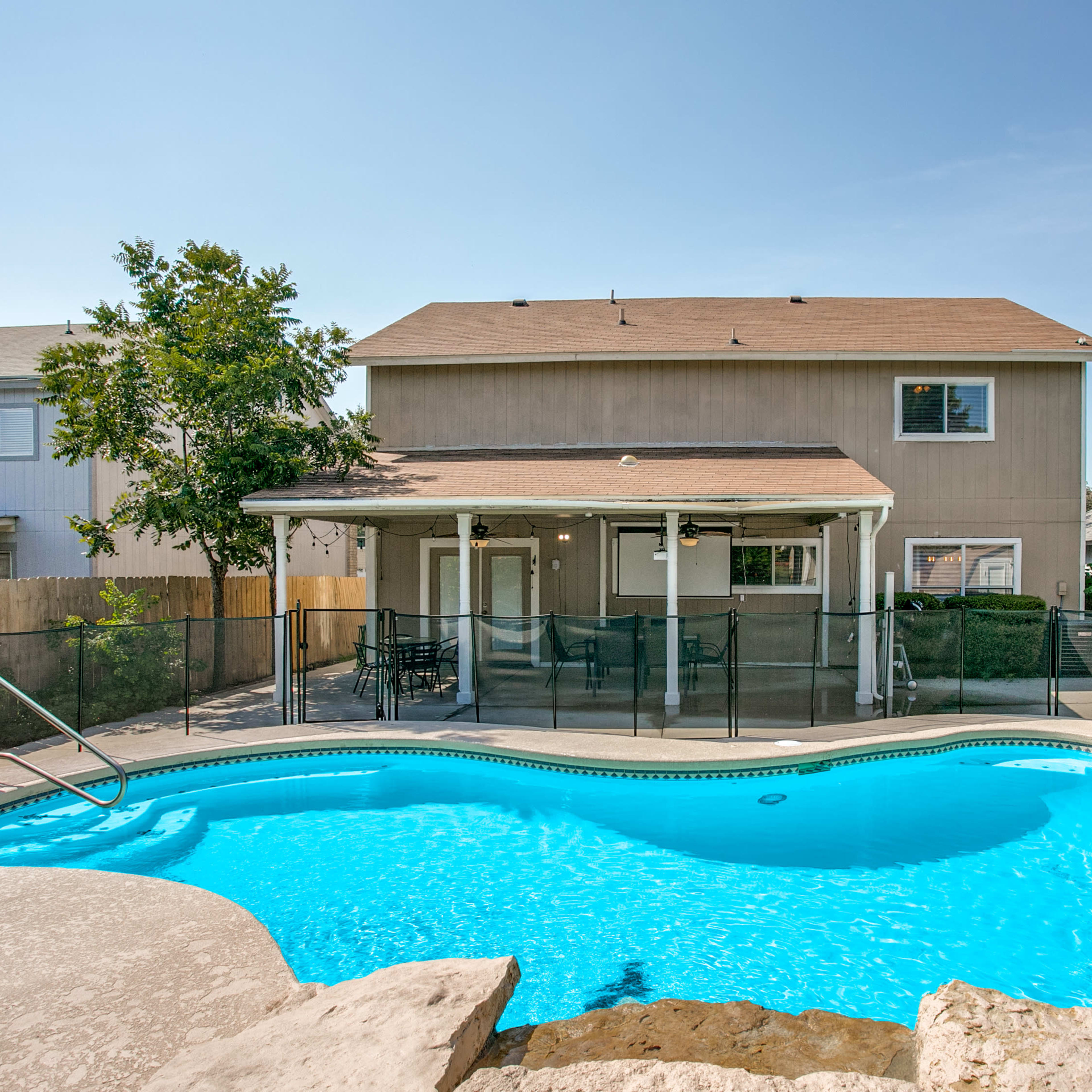A swimming pool is located in the foreground with a fenced patio and a two-story house visible in the background.