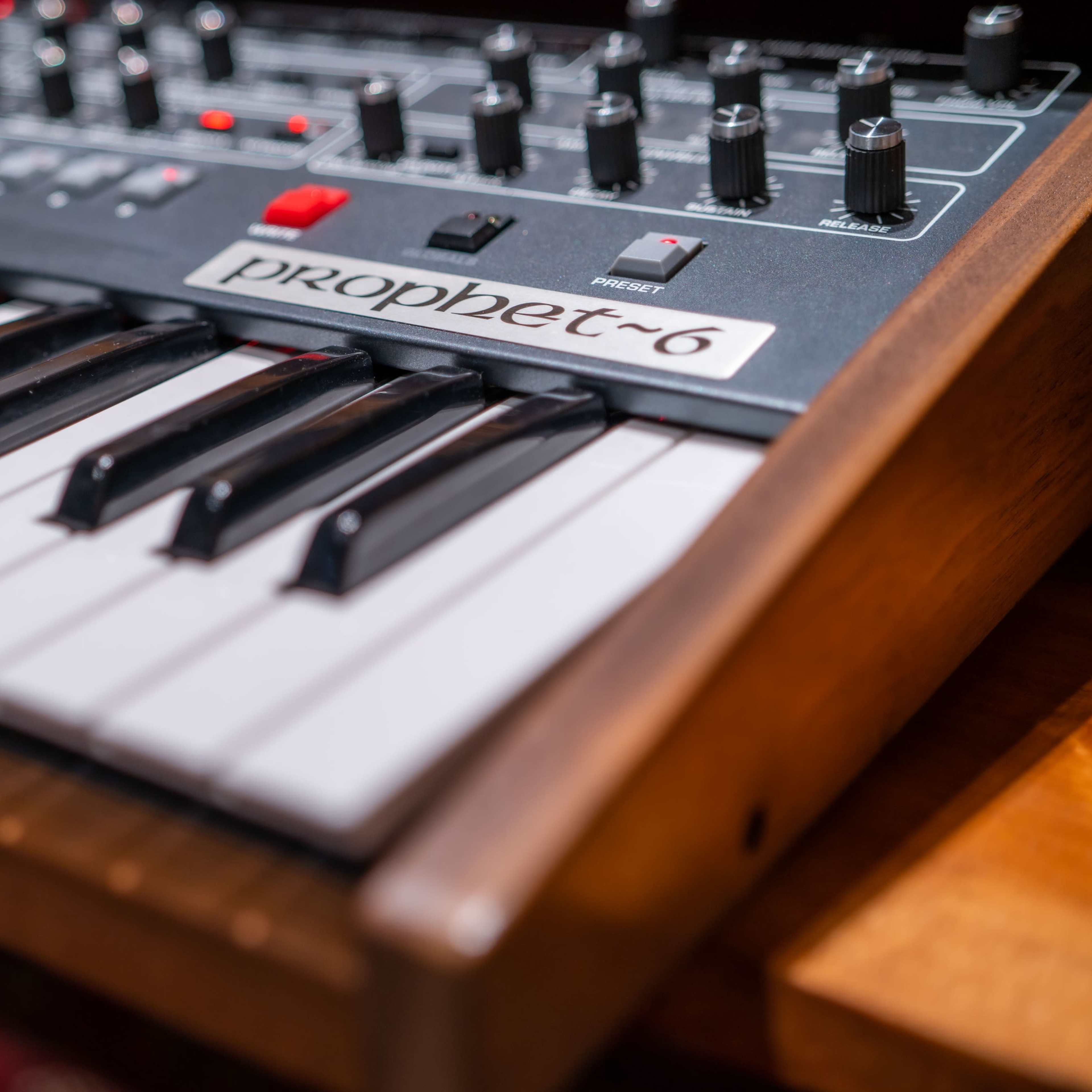 A close-up of a Prophet-6 synthesizer with its keyboard and control panel prominently displayed.