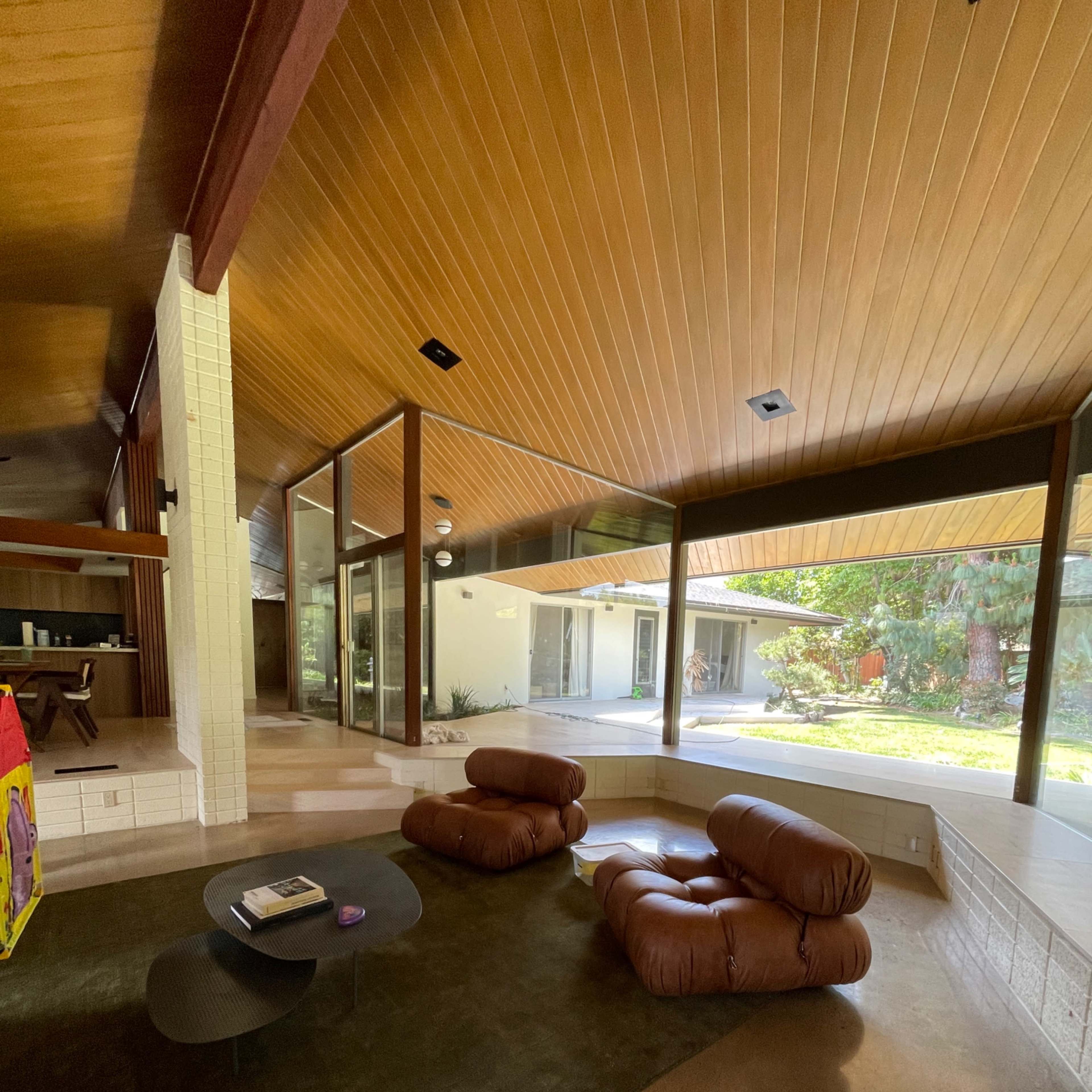 A modern living room featuring two brown lounge chairs, a black coffee table, and large windows that provide a view of a grassy outdoor area.
