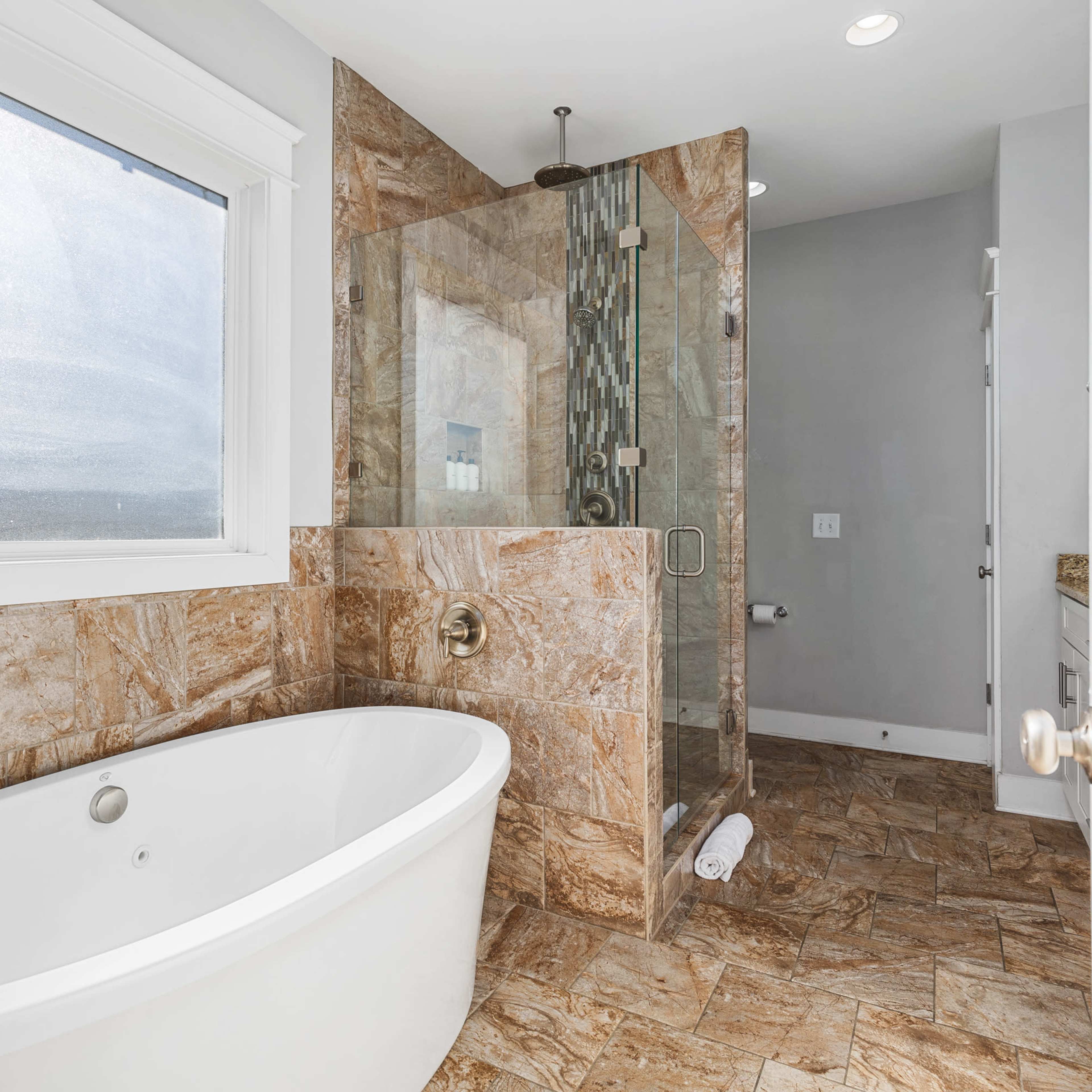 A modern bathroom featuring a freestanding white bathtub, a glass-enclosed shower, and tiled walls and floor.