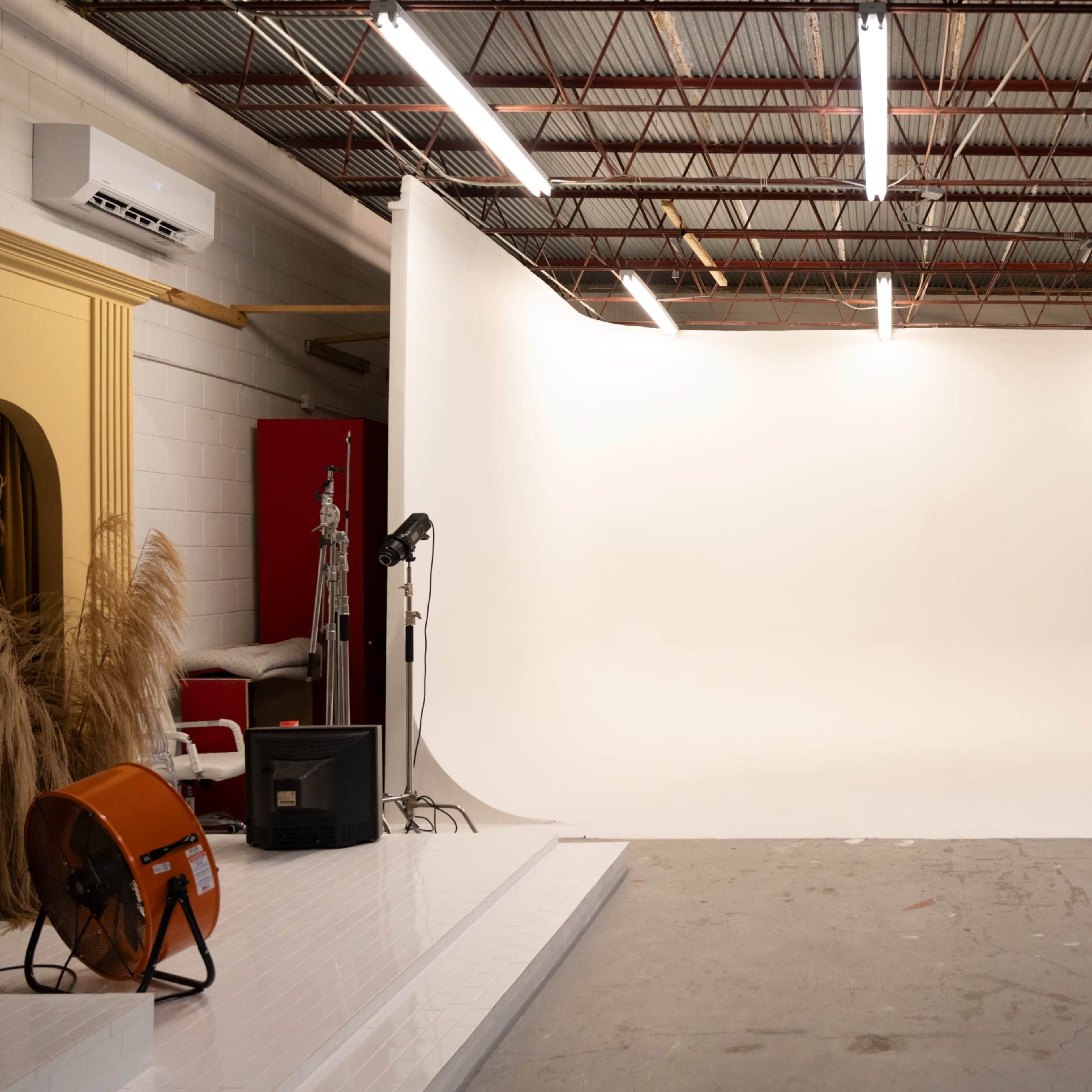 A photography studio with a white backdrop, lighting equipment, and scattered props and furniture.