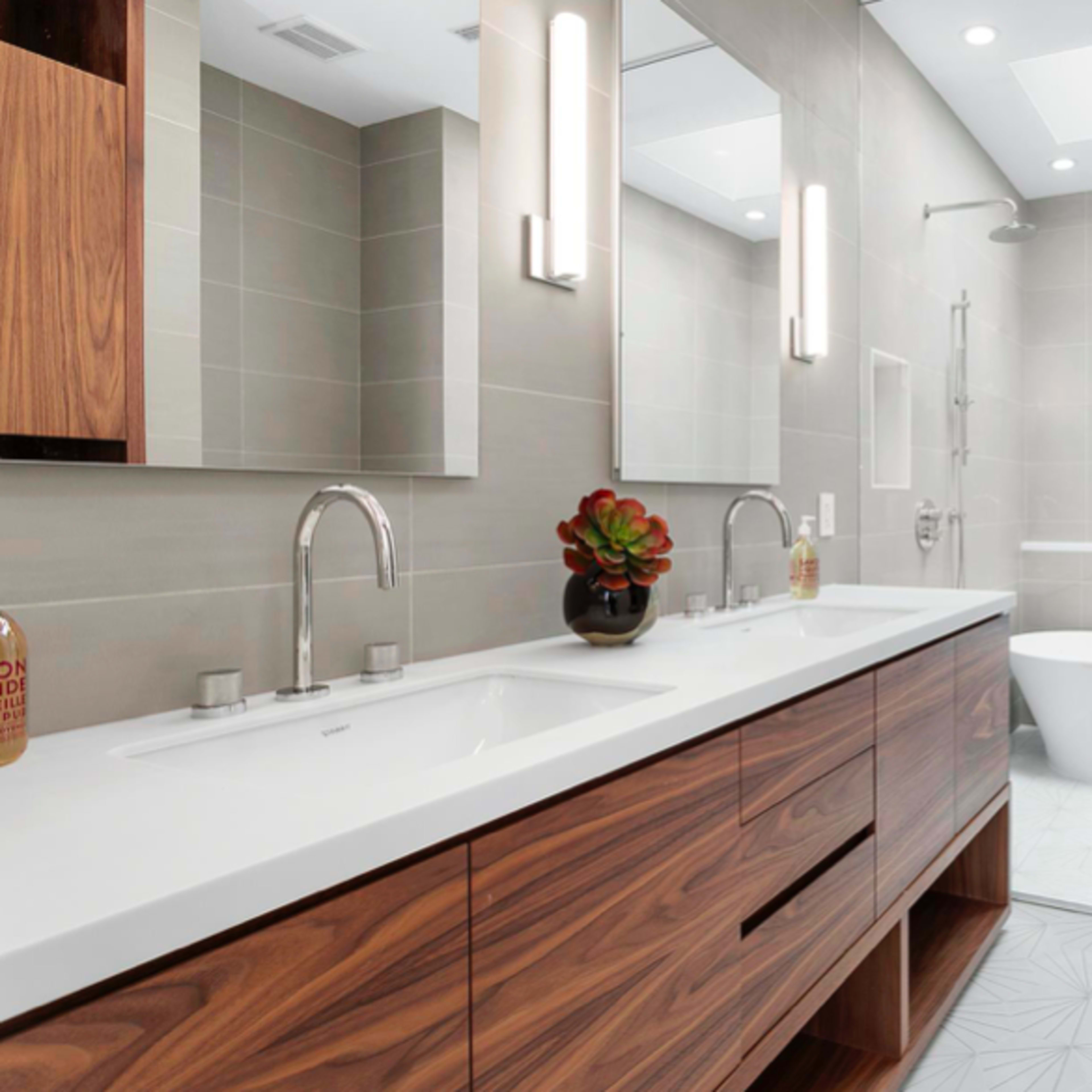 A modern bathroom featuring a double vanity with wooden cabinets, a freestanding bathtub, and a walk-in shower with glass walls.