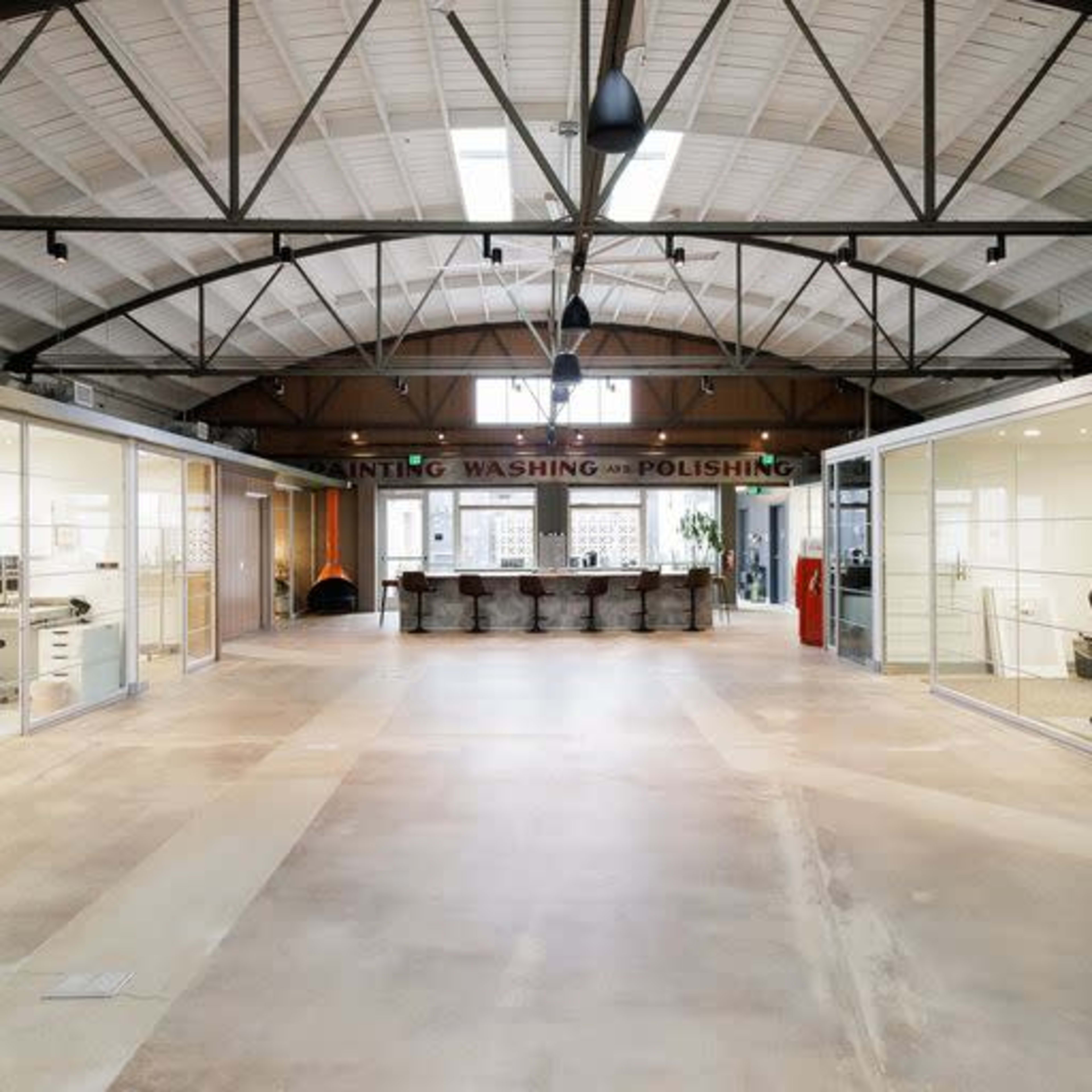 A spacious office area with high ceilings, glass-walled meeting rooms on either side, and a central bar-like counter at the back.