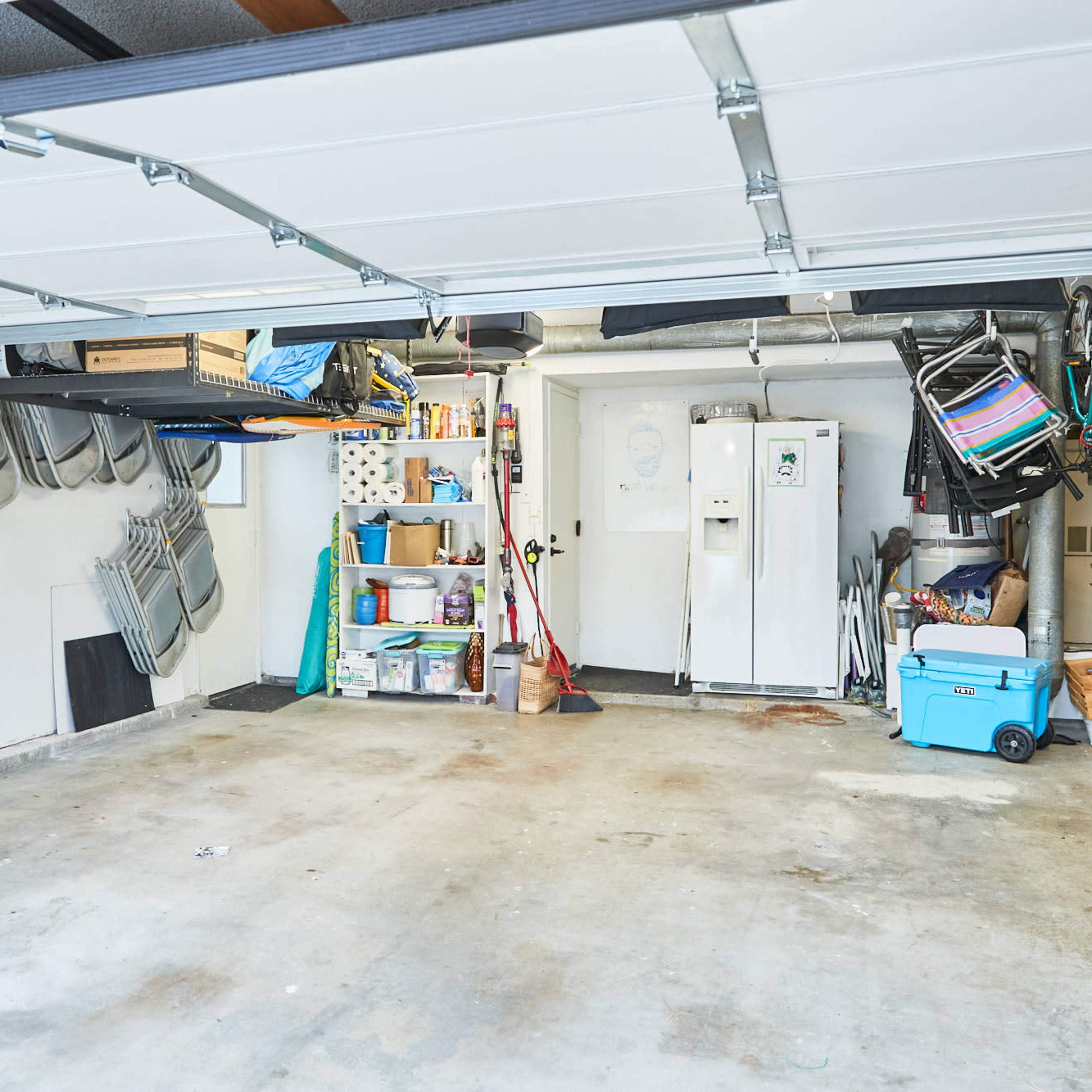 A cluttered garage with a variety of storage items, bicycles, and a refrigerator along the walls.