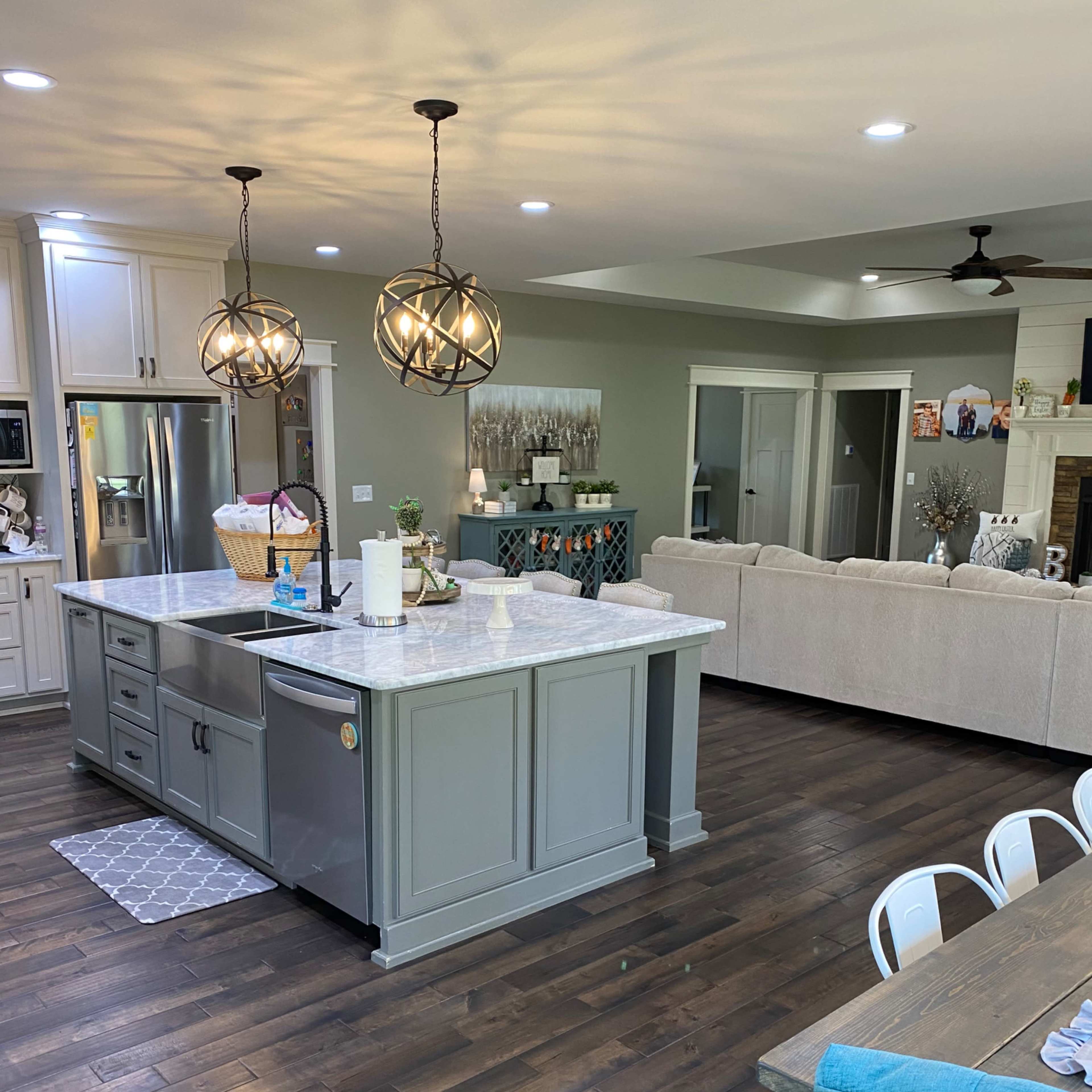 A modern kitchen with an island, pendant lights, and a living area with a sofa and dining table.