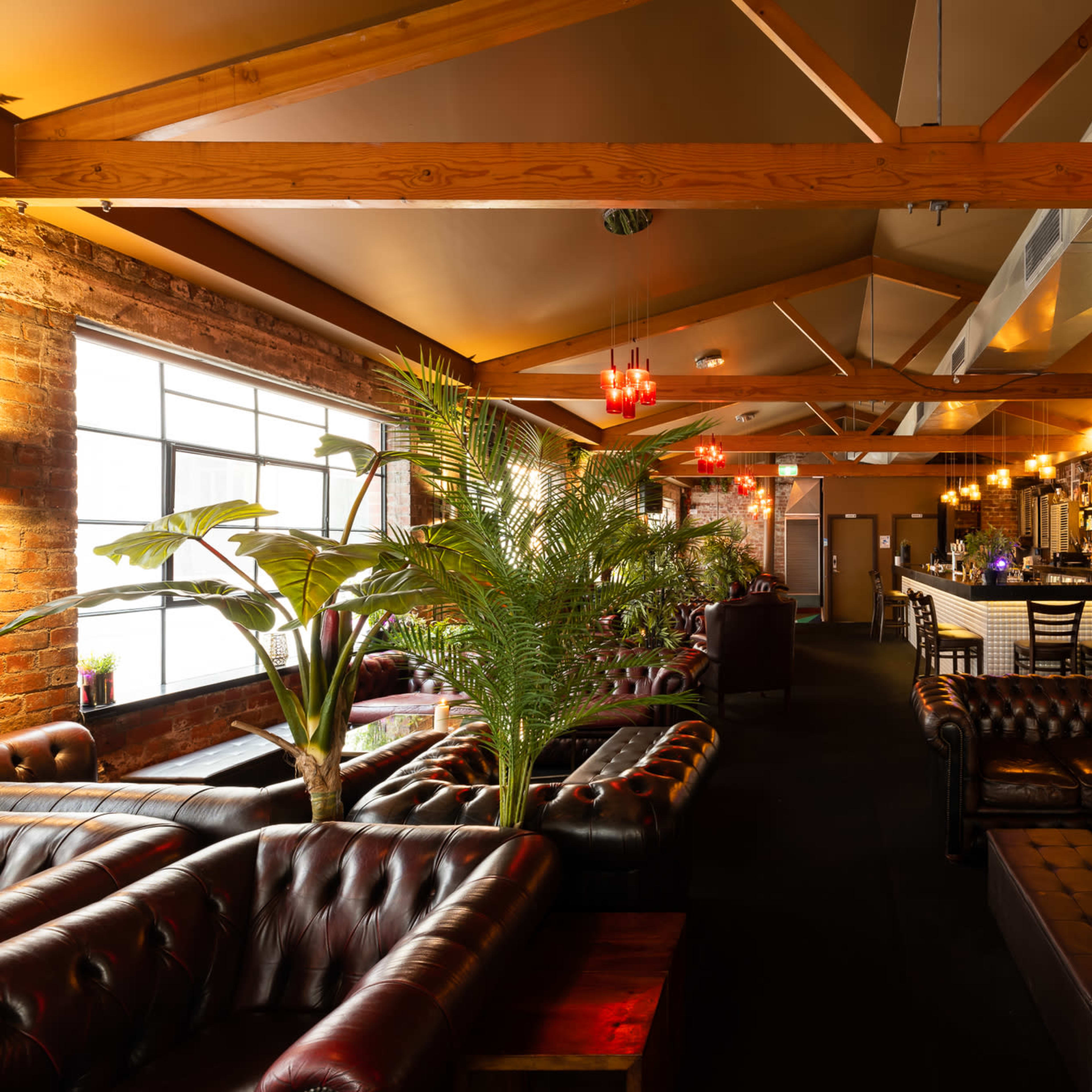 A dimly lit bar interior featuring leather couch seating, wooden beams, and a well-stocked bar in the background.