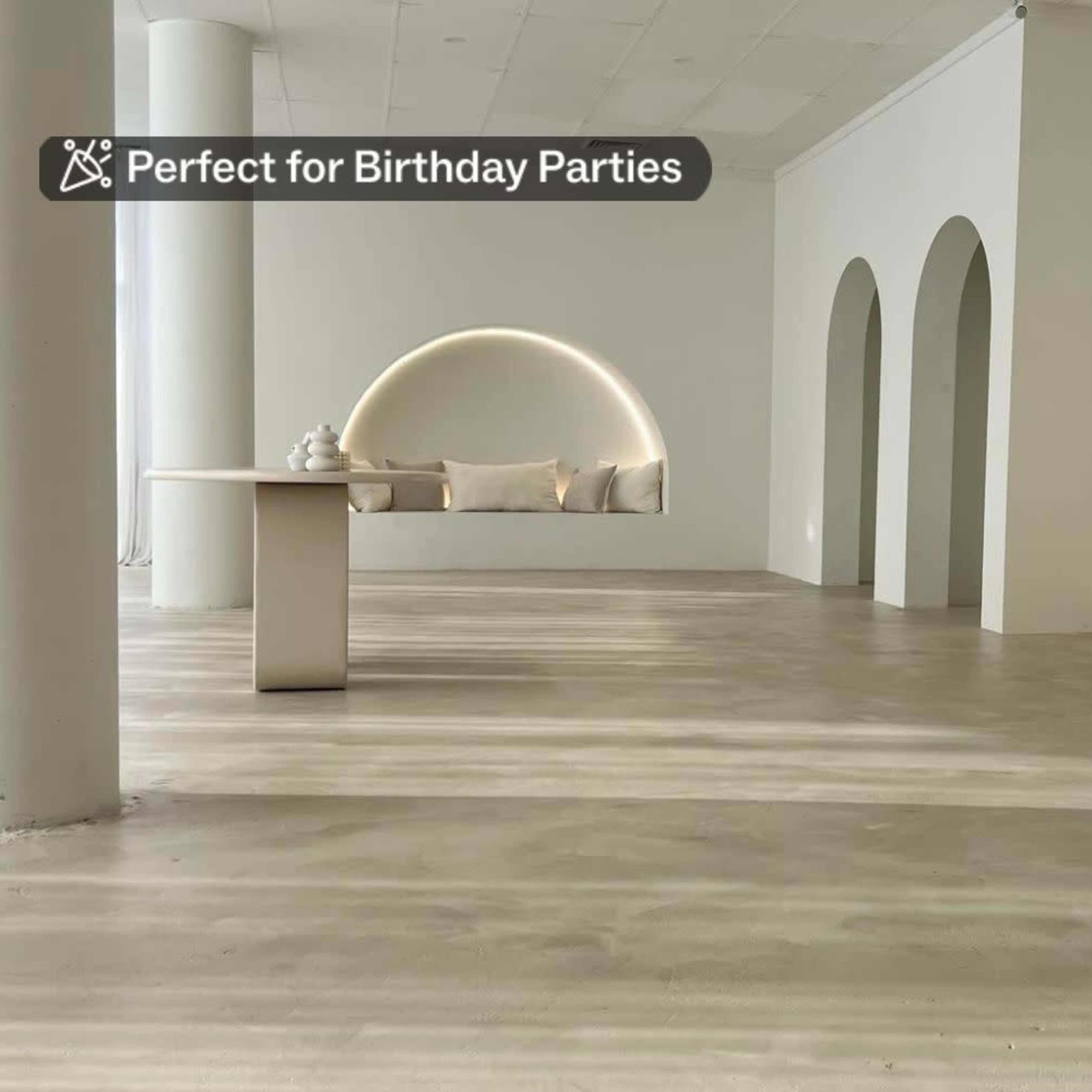 A minimalistic interior space with a large mirror, a simple table, and archways on the walls, featuring a light-colored floor and soft seating.