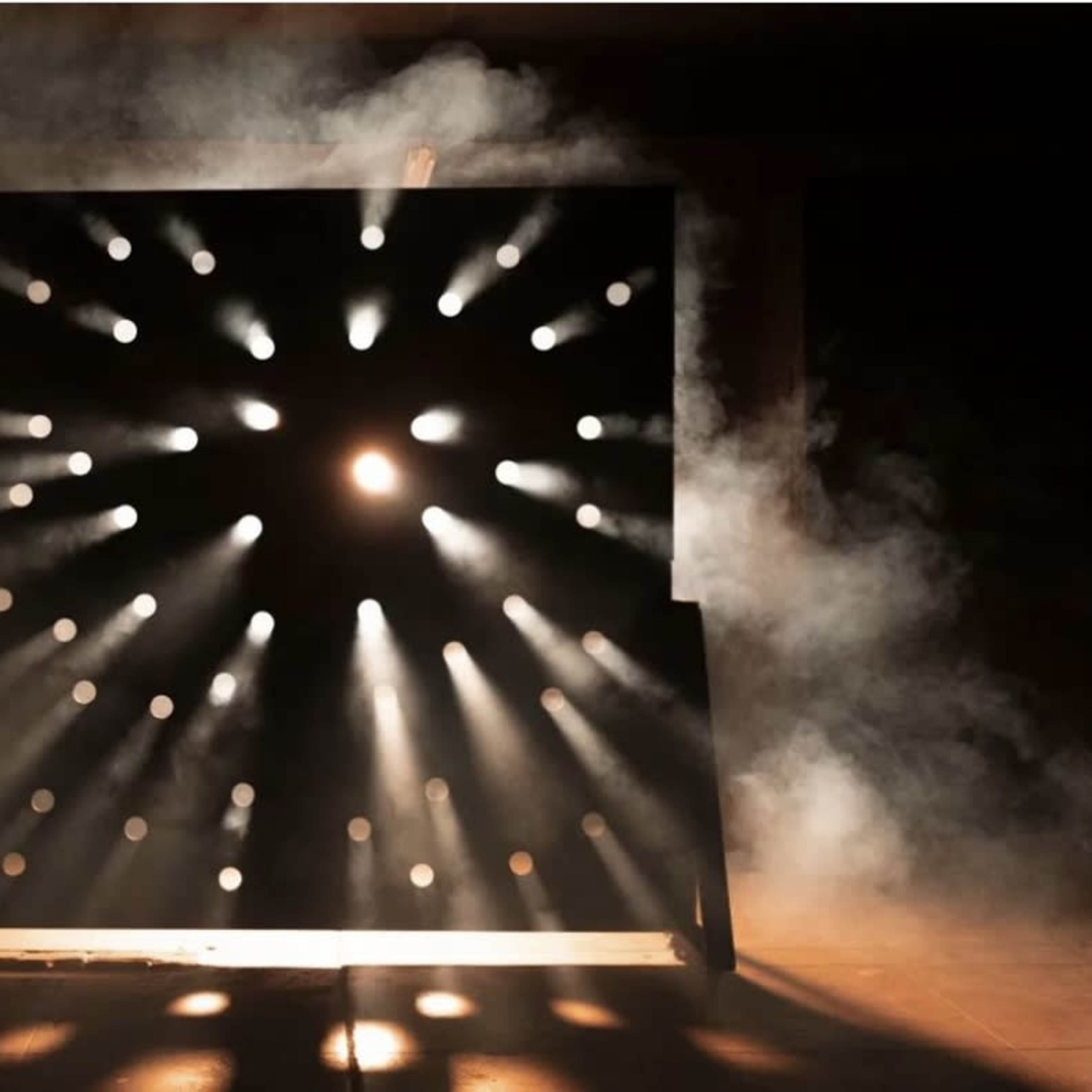 A large black panel emits beams of light in a smoky environment, creating a dramatic visual effect.