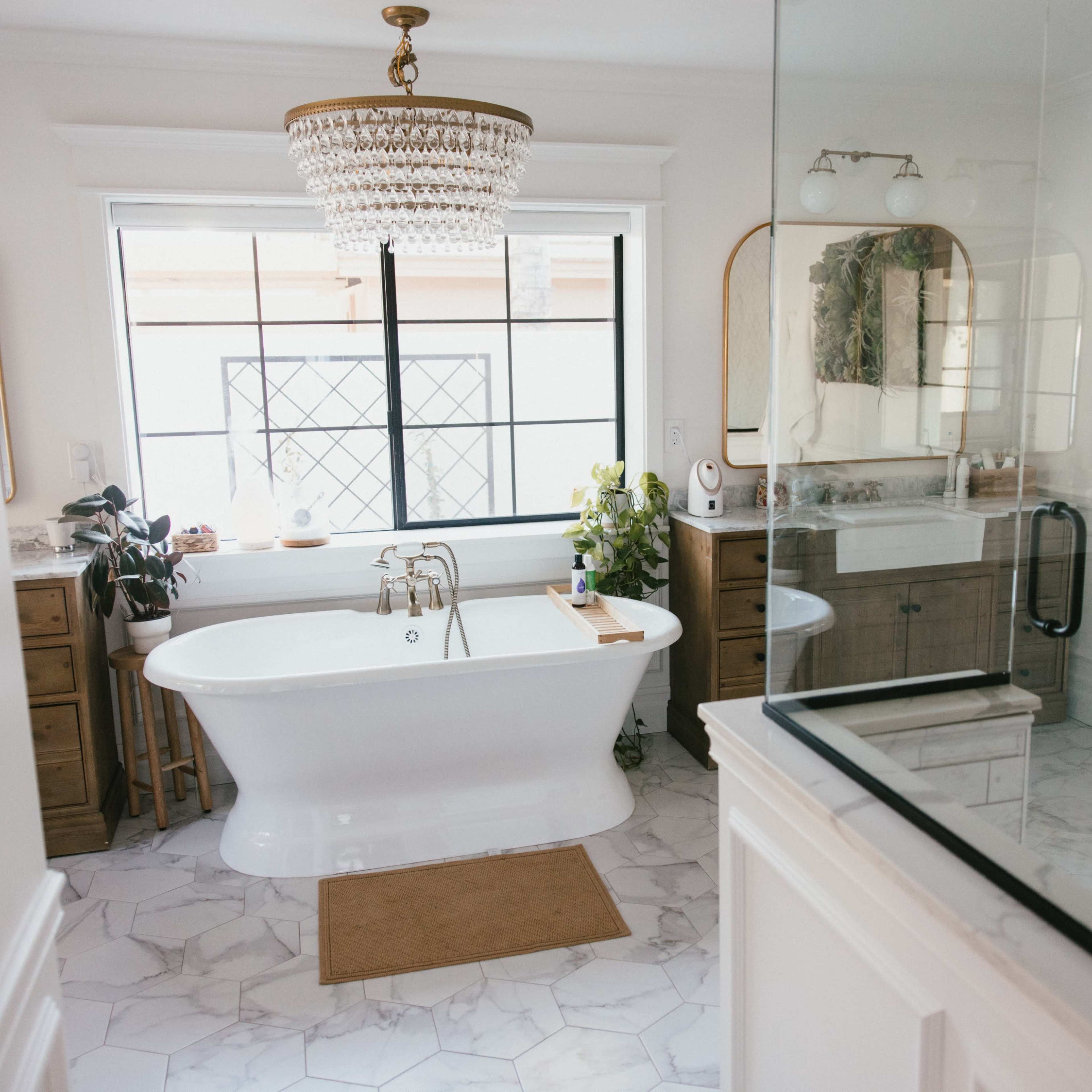 A bathroom featuring a freestanding bathtub, a large window with a view, and a glass shower enclosure alongside wooden cabinets and a sink.