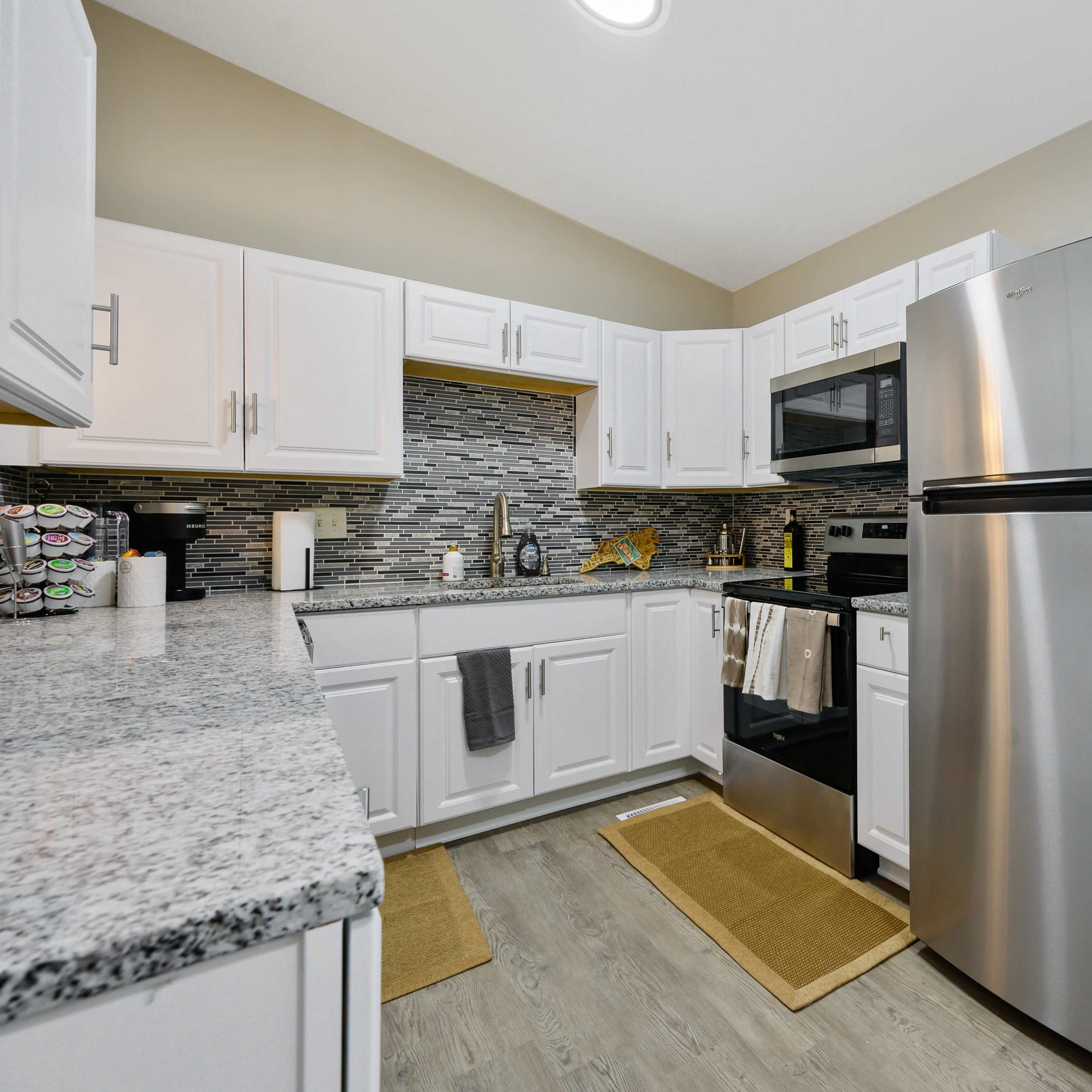 A modern kitchen featuring white cabinetry, a stainless steel refrigerator, and a door leading to a deck area.