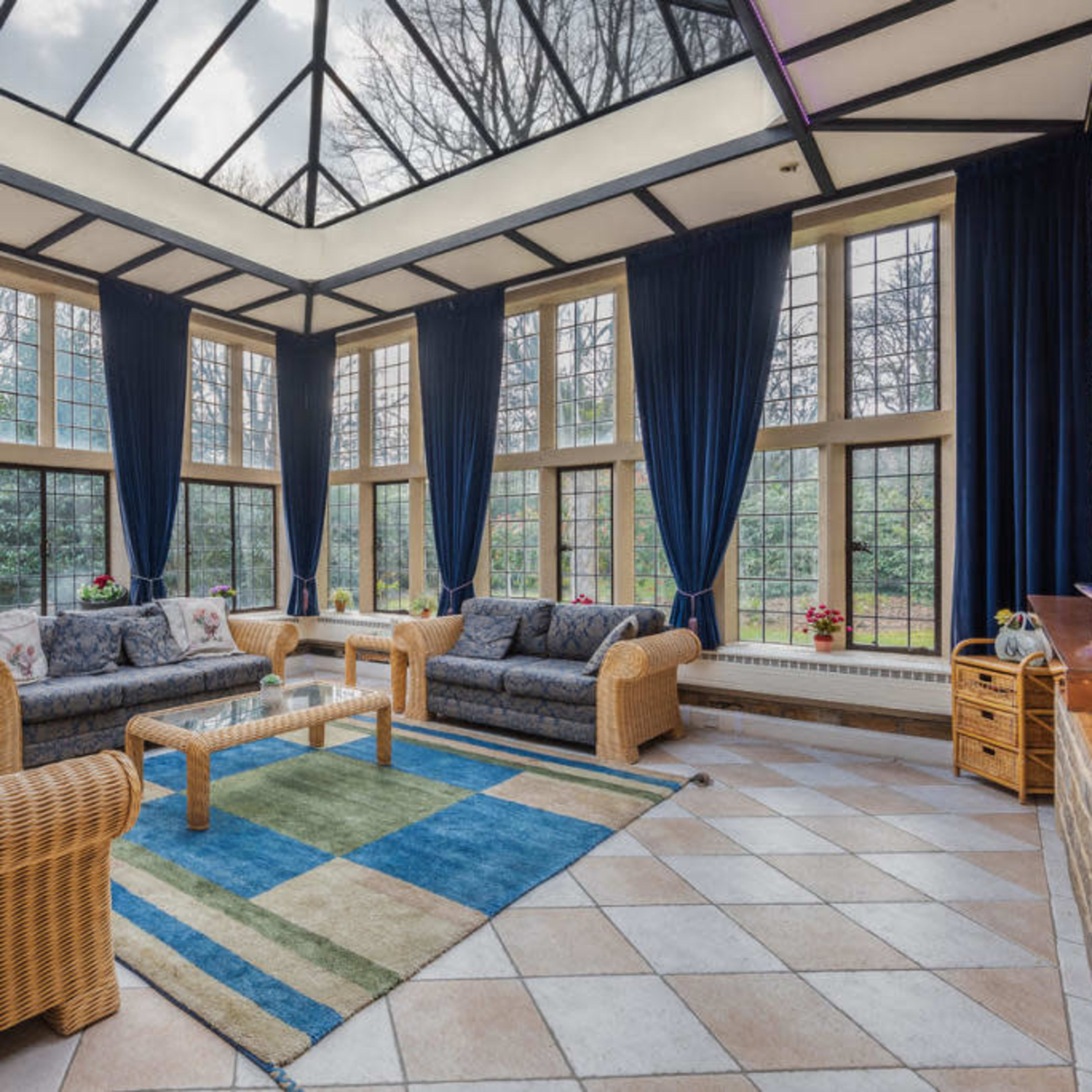 A sunroom filled with wicker furniture, large windows, and a tiled floor, illuminated by natural light.