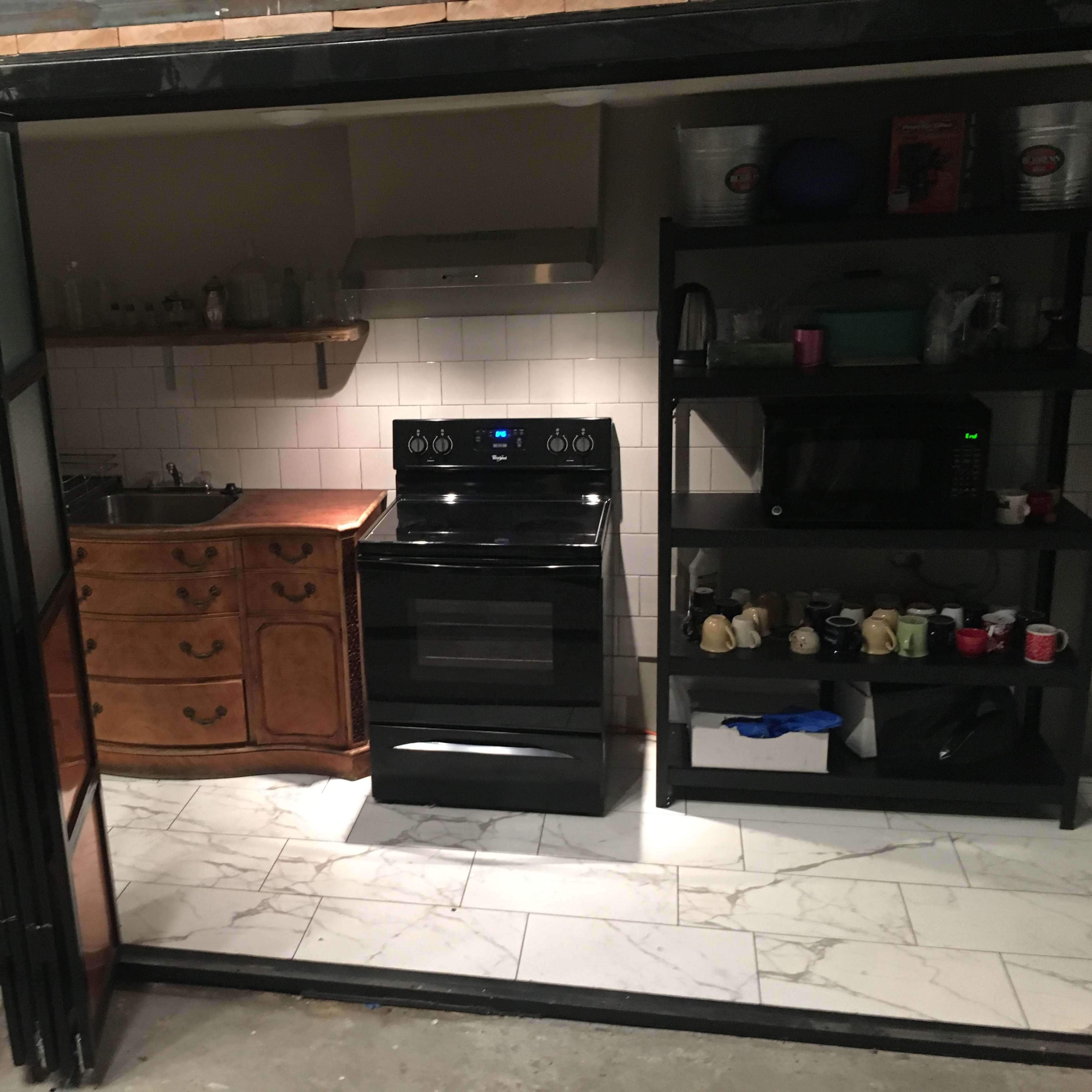 A modern kitchen with a black stove and oven, a stainless steel range hood, a wooden cabinet, and various kitchen appliances on black shelves.