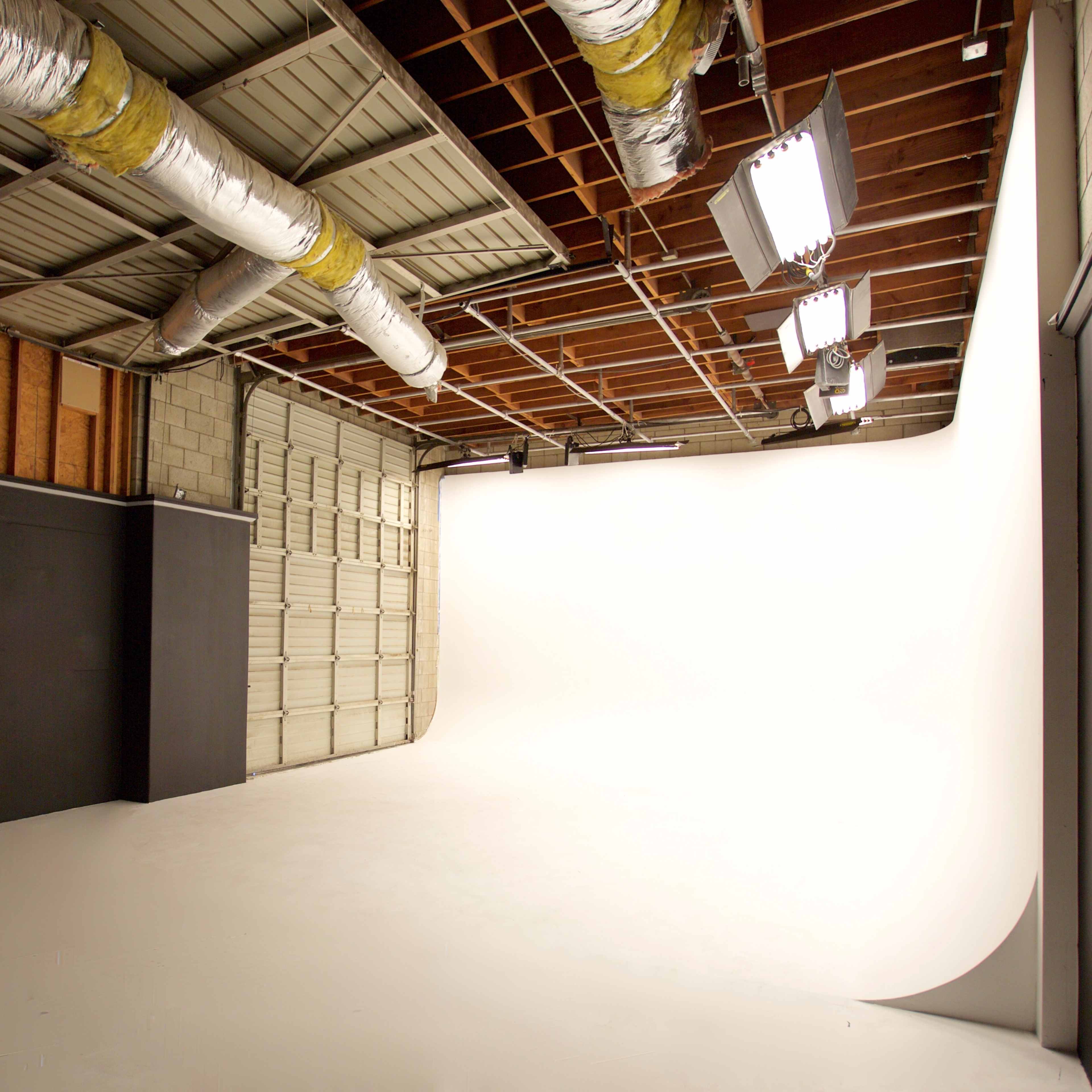 A spacious photography studio with a seamless white backdrop and various lighting fixtures overhead.