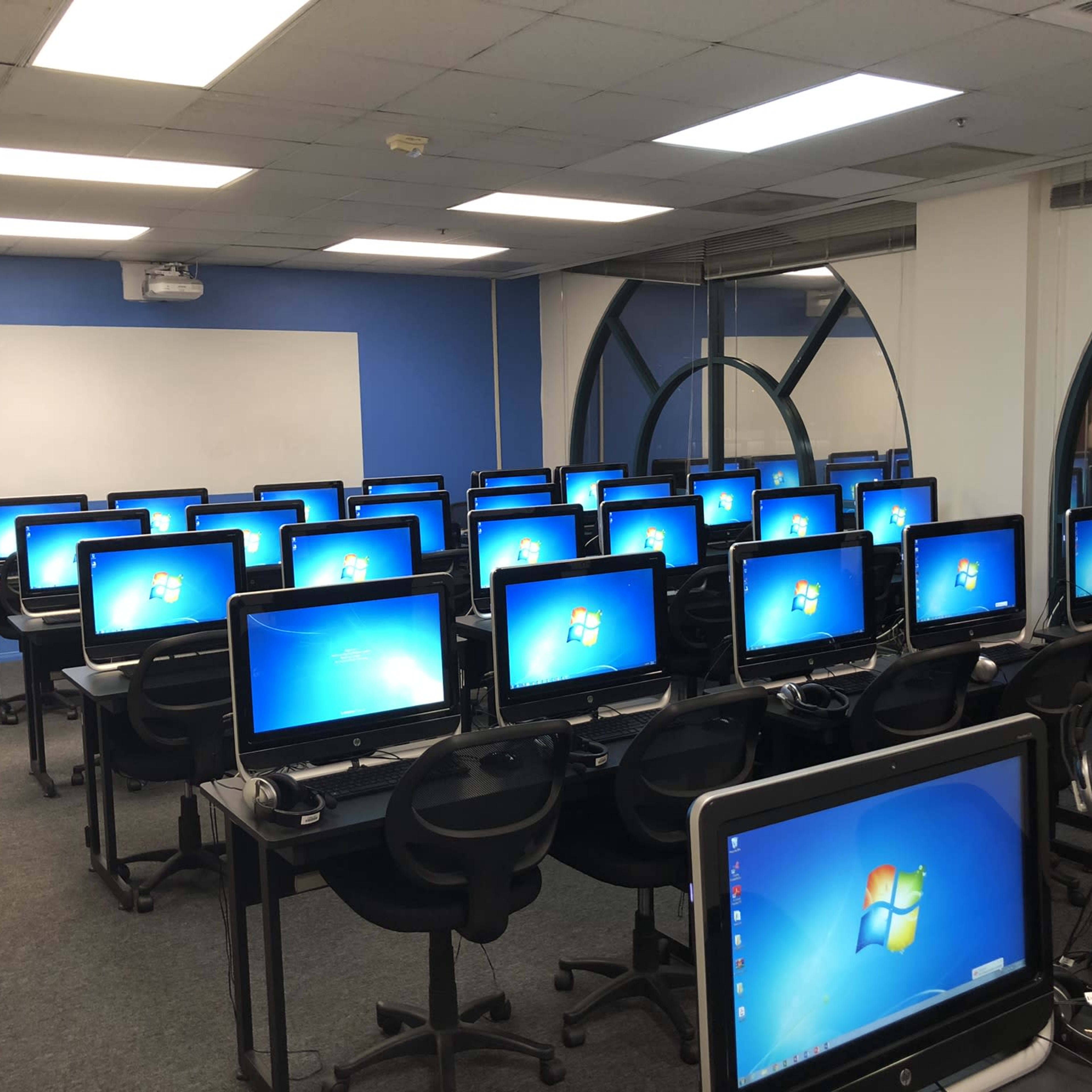 A computer lab with multiple desktop computers arranged in rows, each featuring a Windows login screen.